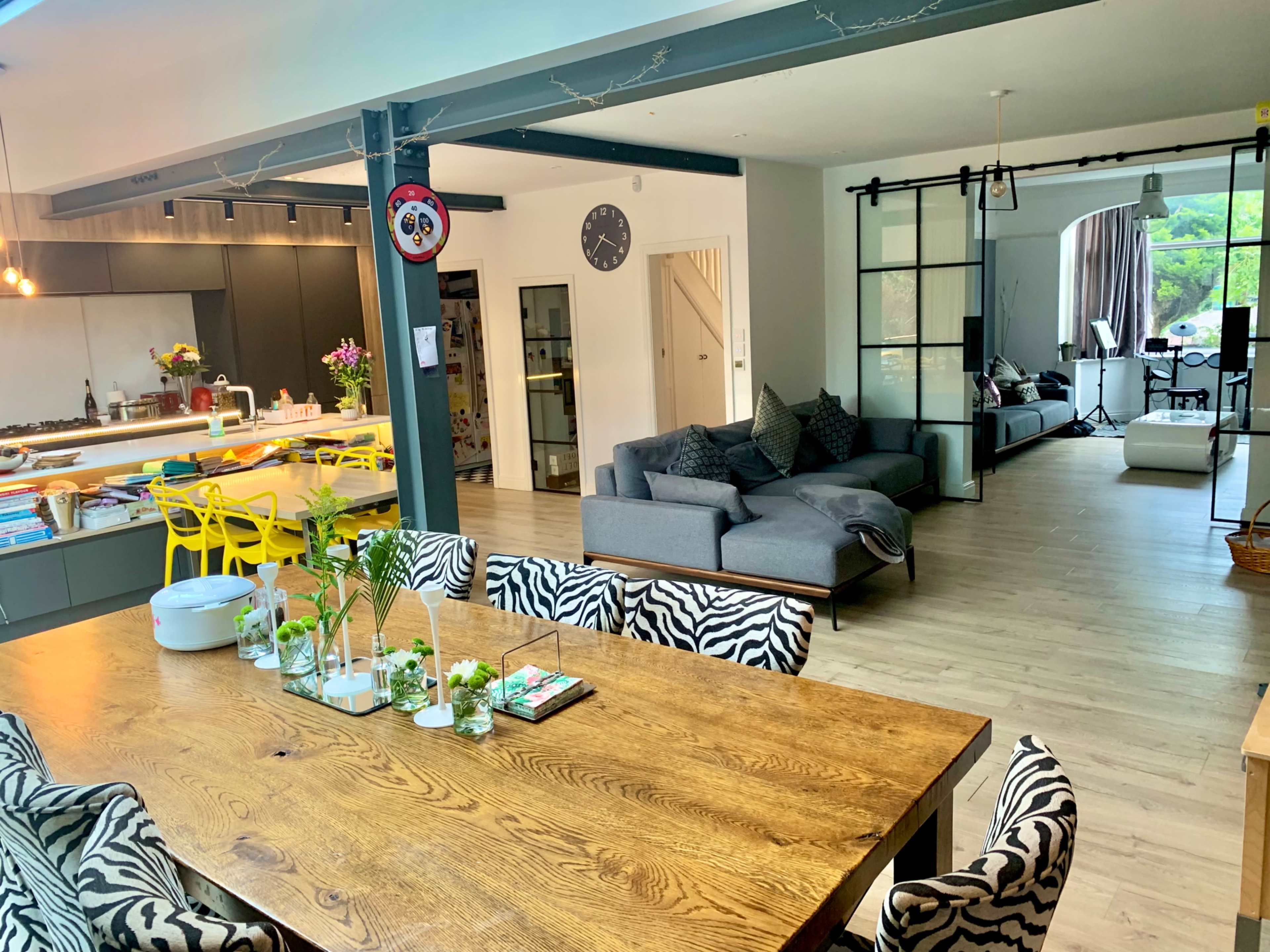 An open-concept living space featuring a dining area with a wooden table surrounded by zebra-print chairs and a modern lounge area with a gray sofa and large windows.