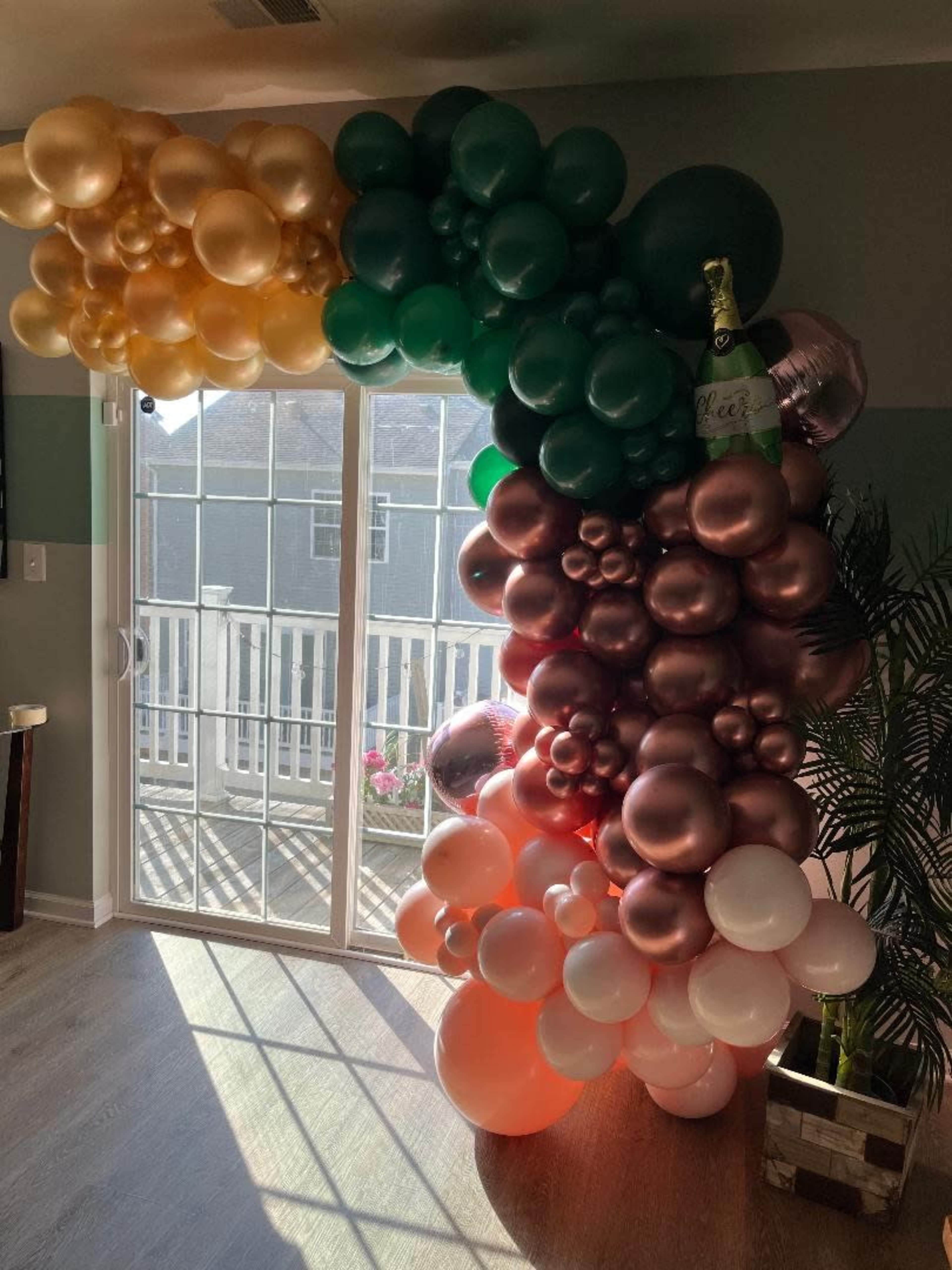 A large balloon arch in various colors stands against a sliding glass door, allowing sunlight to illuminate the space.