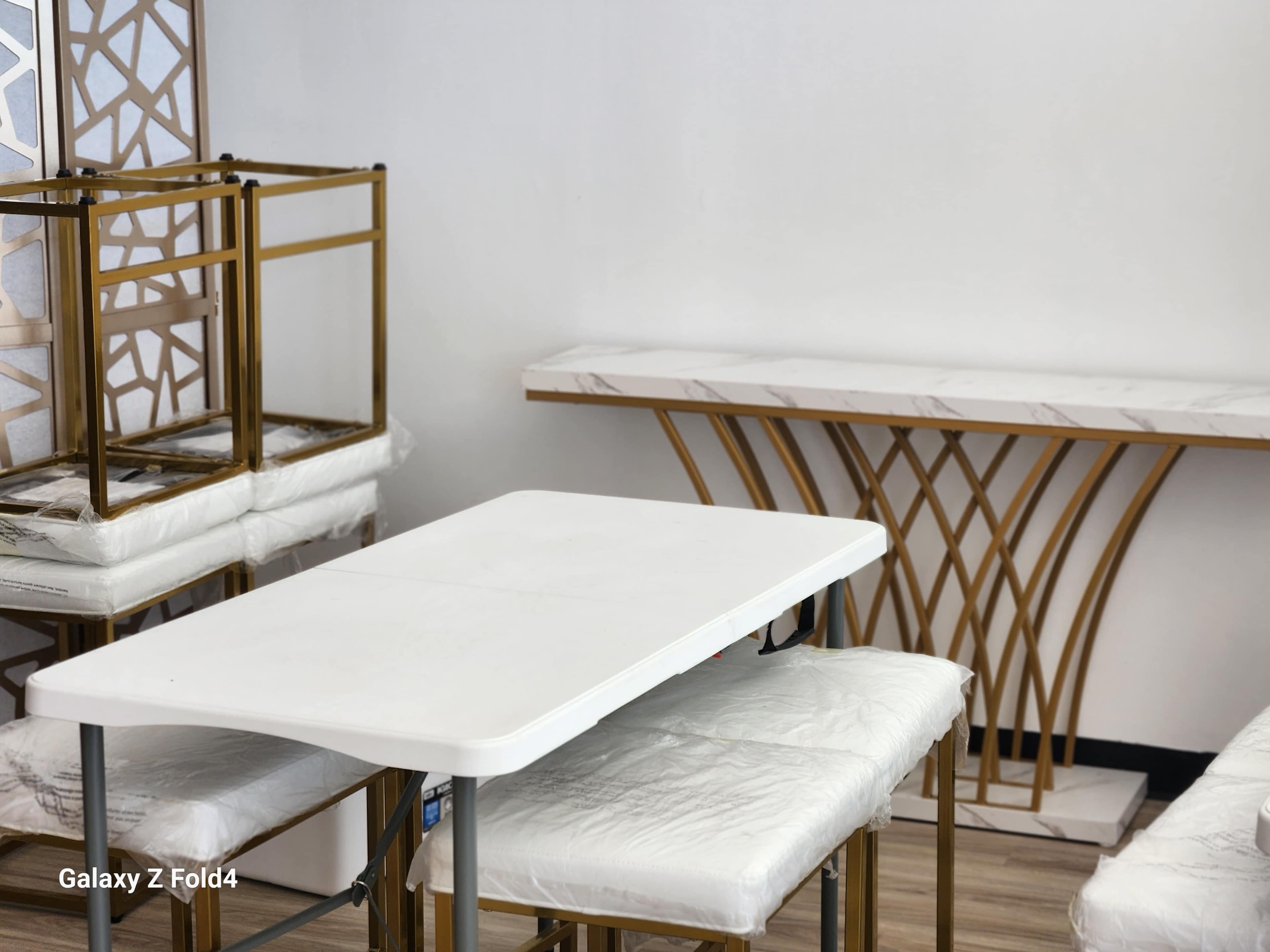 A white table with four cushioned chairs is positioned next to a marble-topped console table in a room with decorative gold accents.