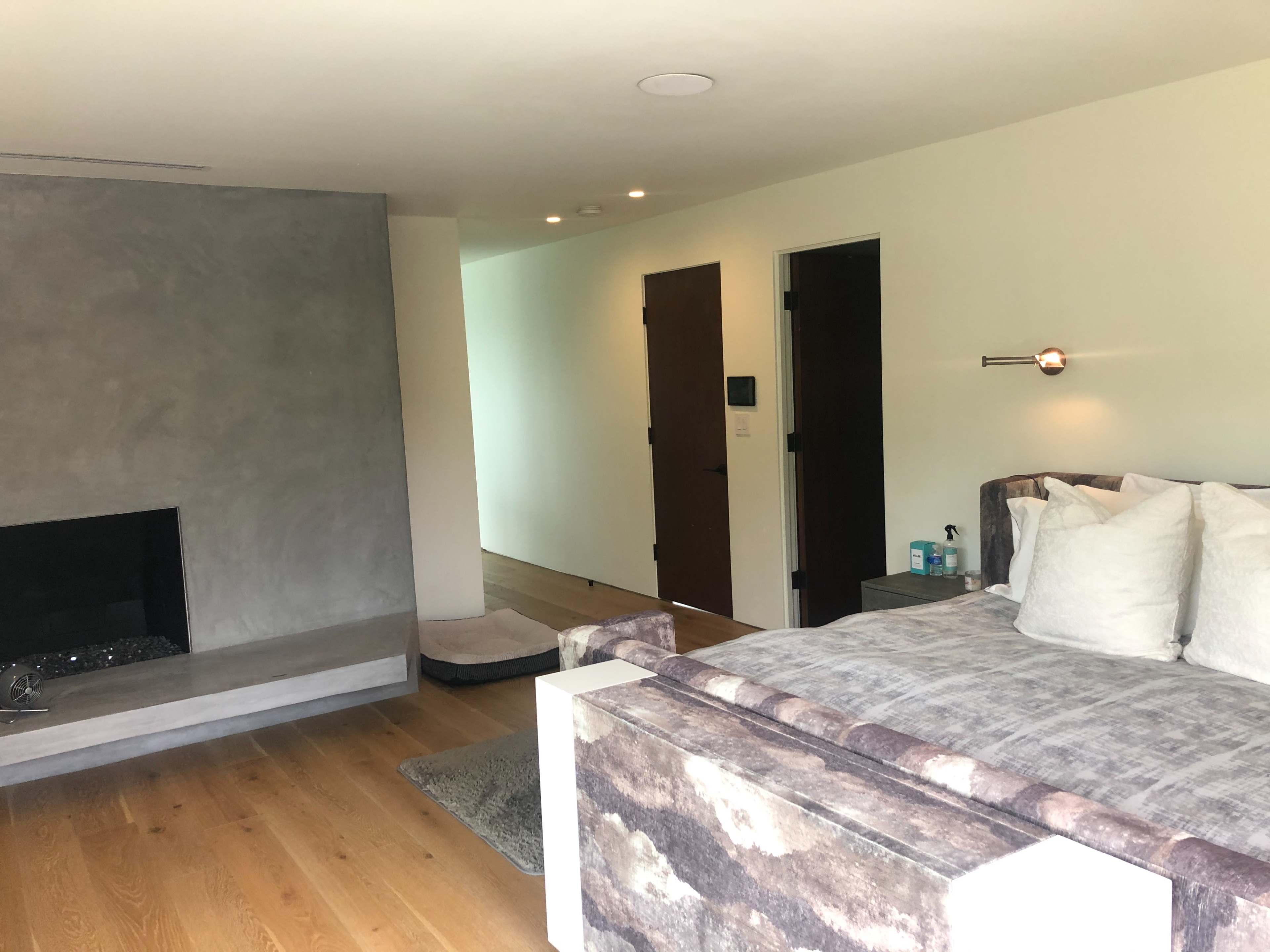 A minimalist bedroom featuring a large bed, a fireplace, and a doorway leading to another room.