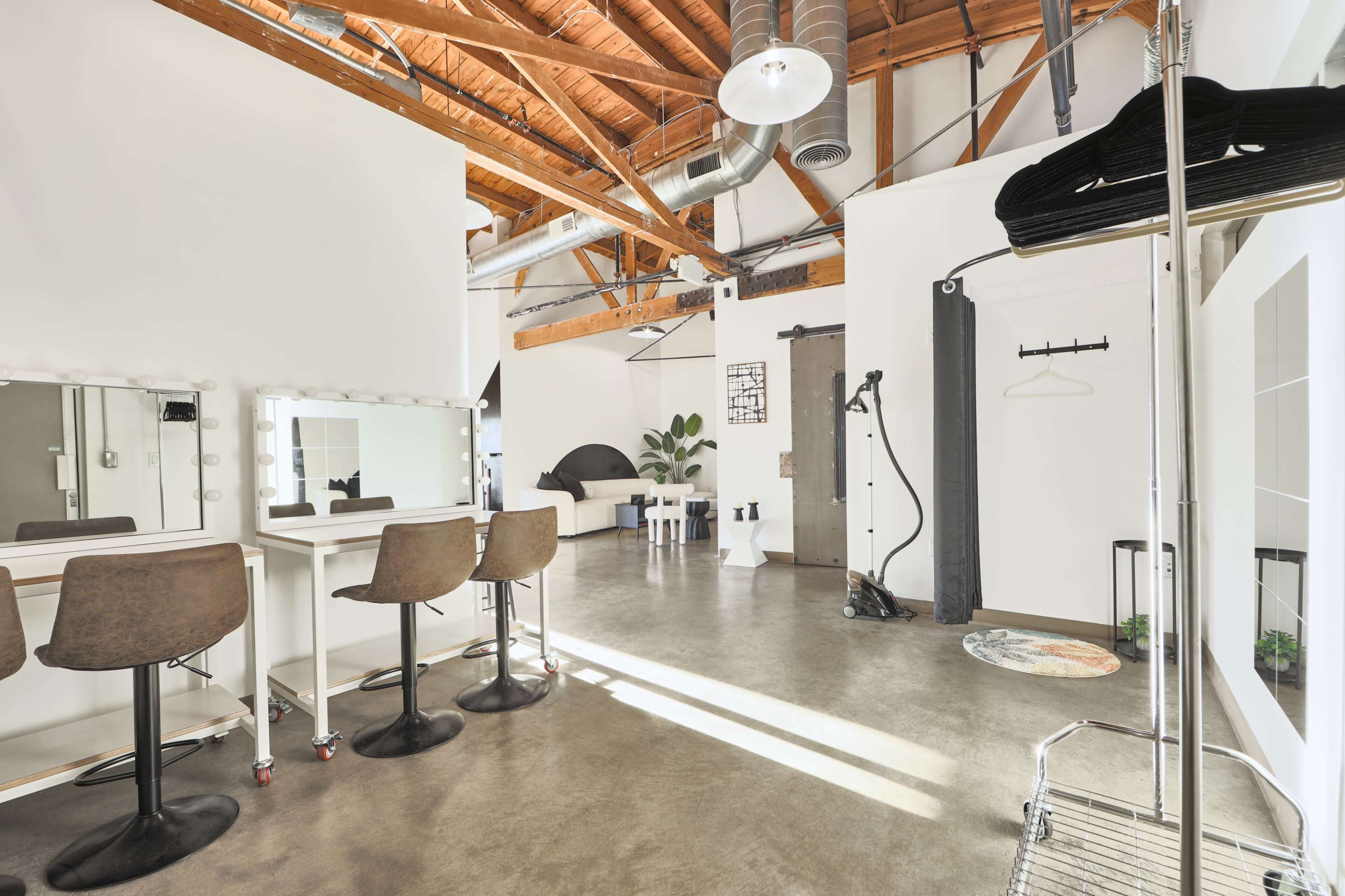 A modern studio space with a concrete floor, exposed wooden beams, a seating area with mirrors, and various equipment along the walls.