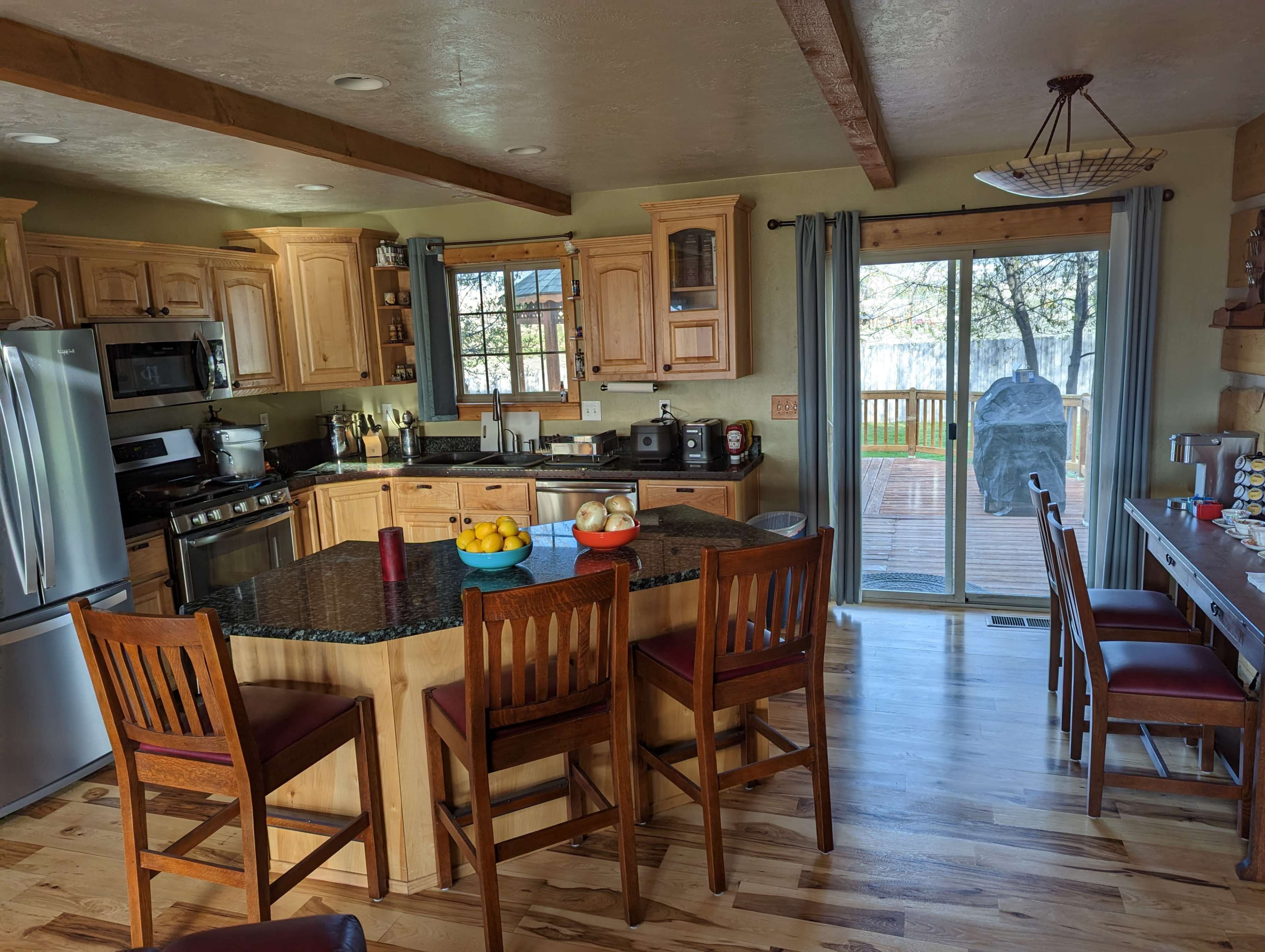 A spacious kitchen features wooden cabinets, a large island with seating for four, and sliding glass doors that lead to an outdoor deck.