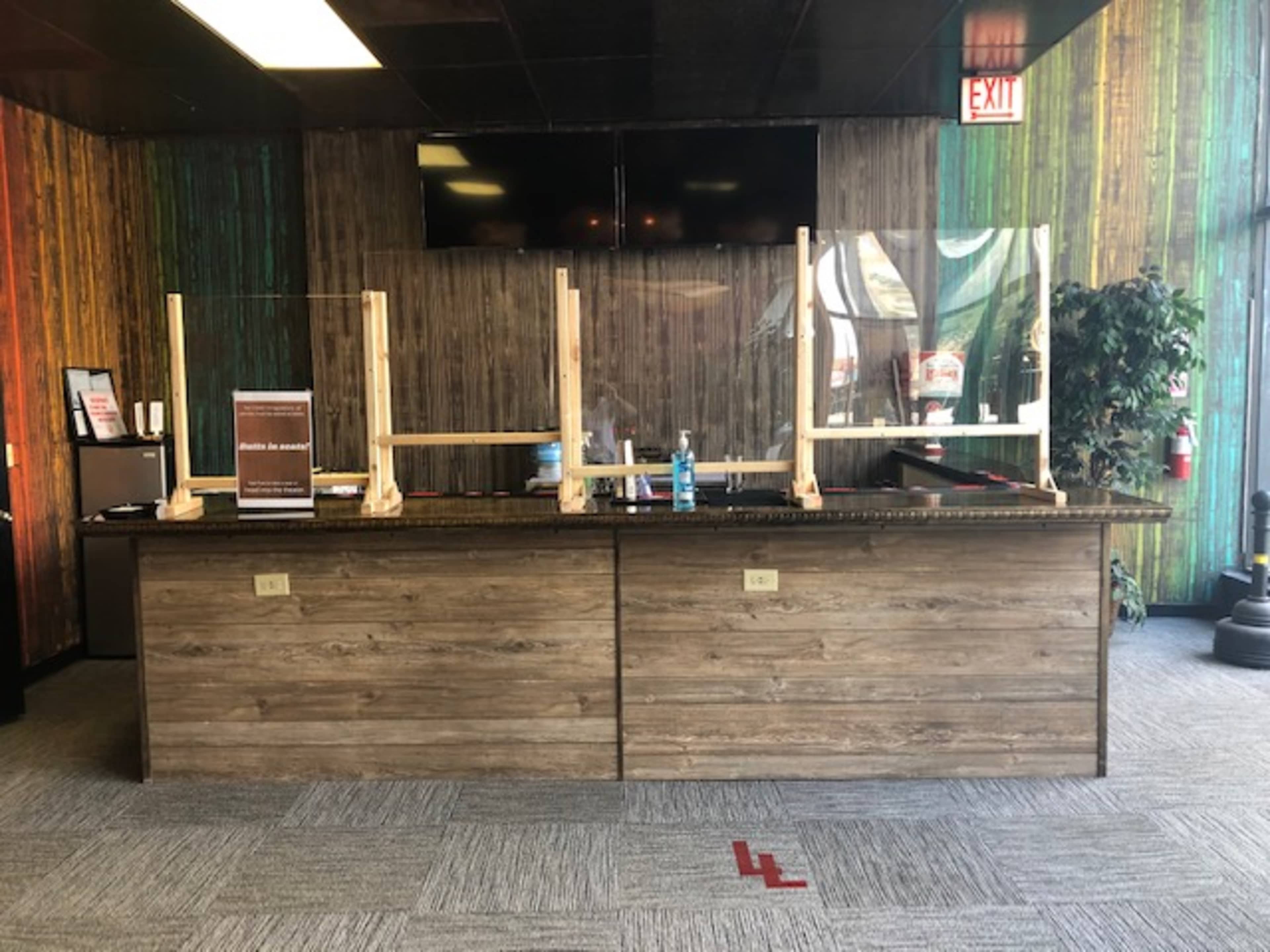 A reception area with a wooden counter, transparent acrylic barriers, and a plant, set against a colorful wooden wall.