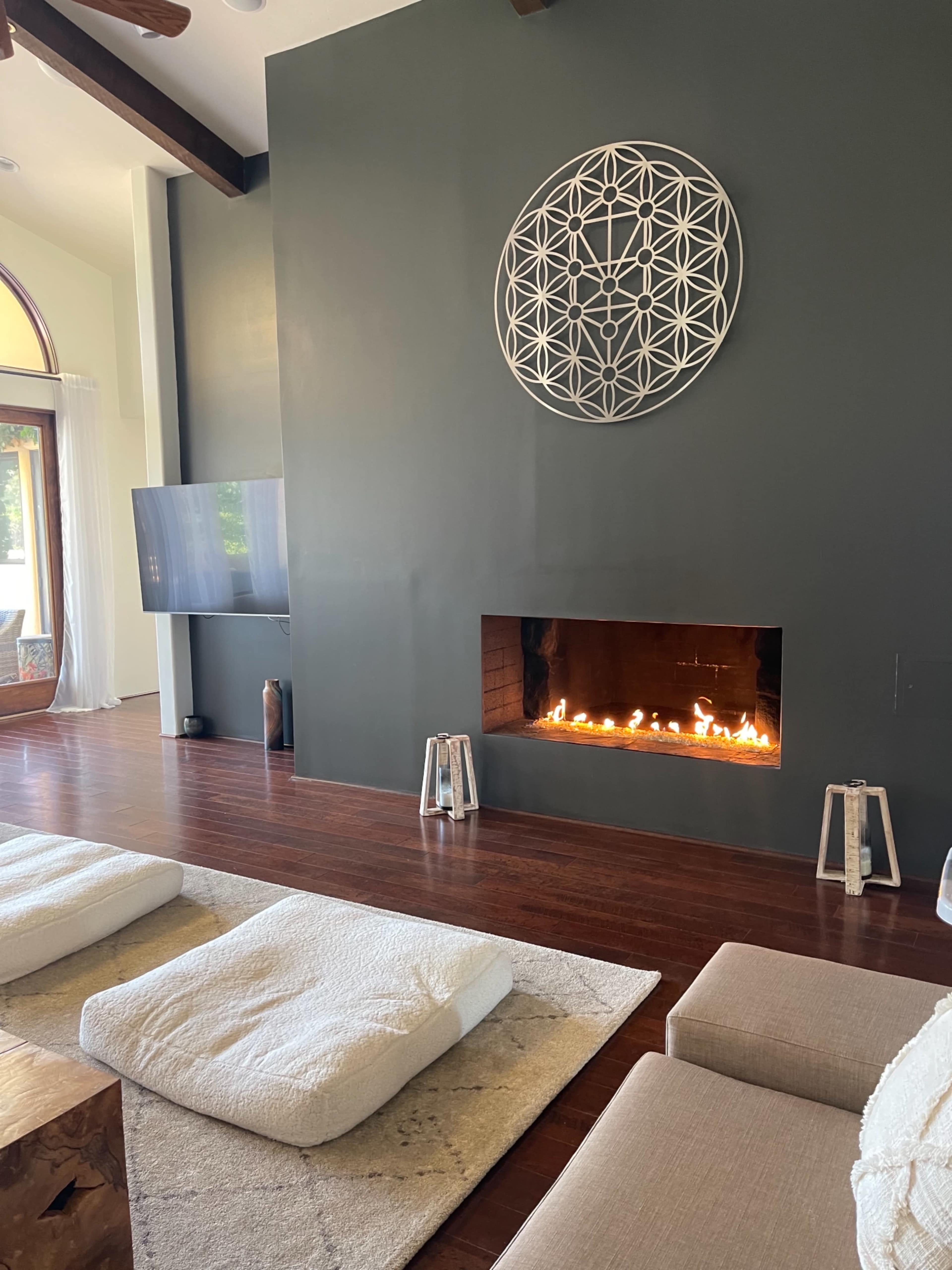 The room features a modern fireplace set into a dark wall, with minimalist seating and large windows allowing natural light to enter.