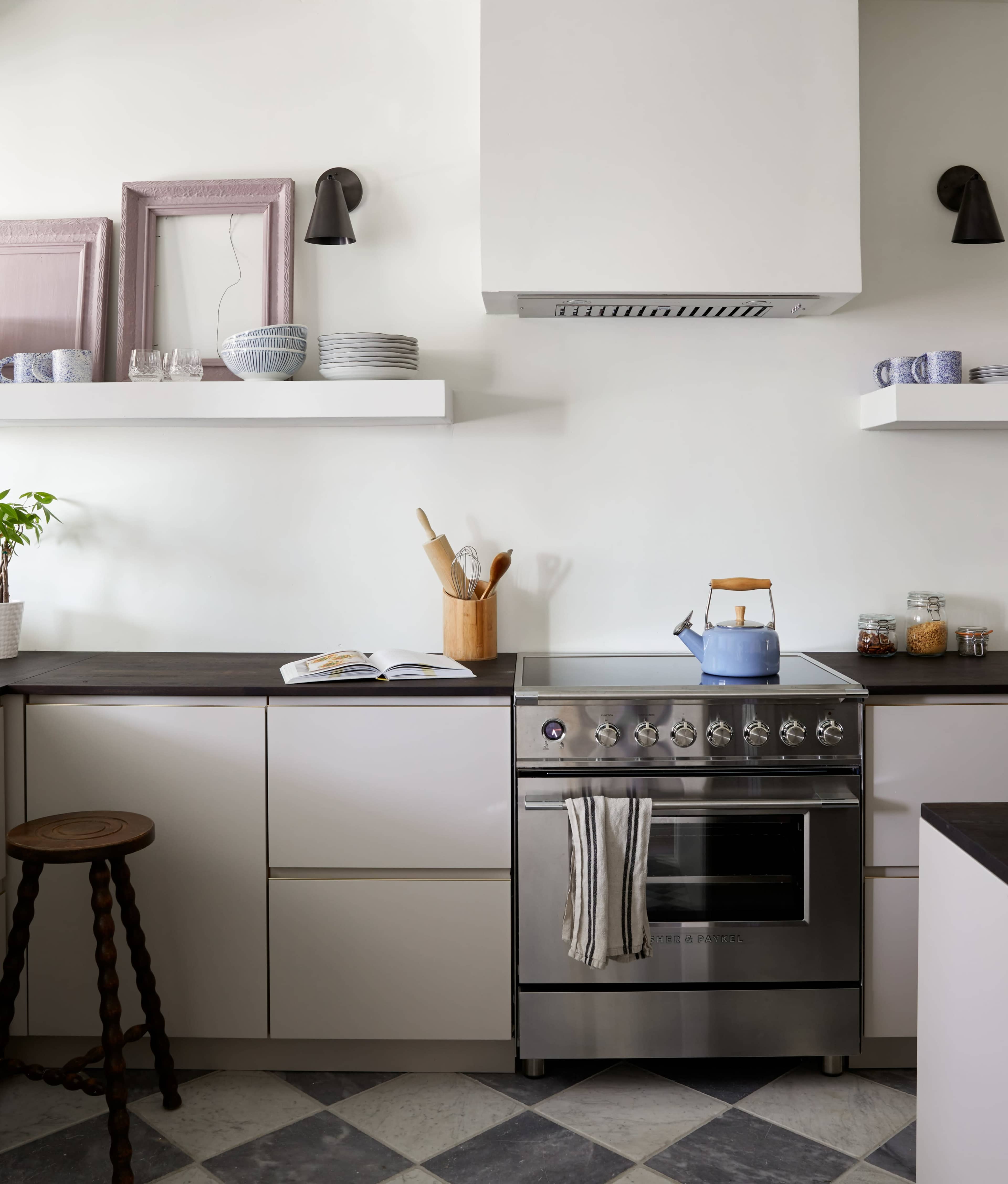 A modern kitchen features a stainless steel stove, wooden utensils in a container, and open shelves displaying dishware and plants.