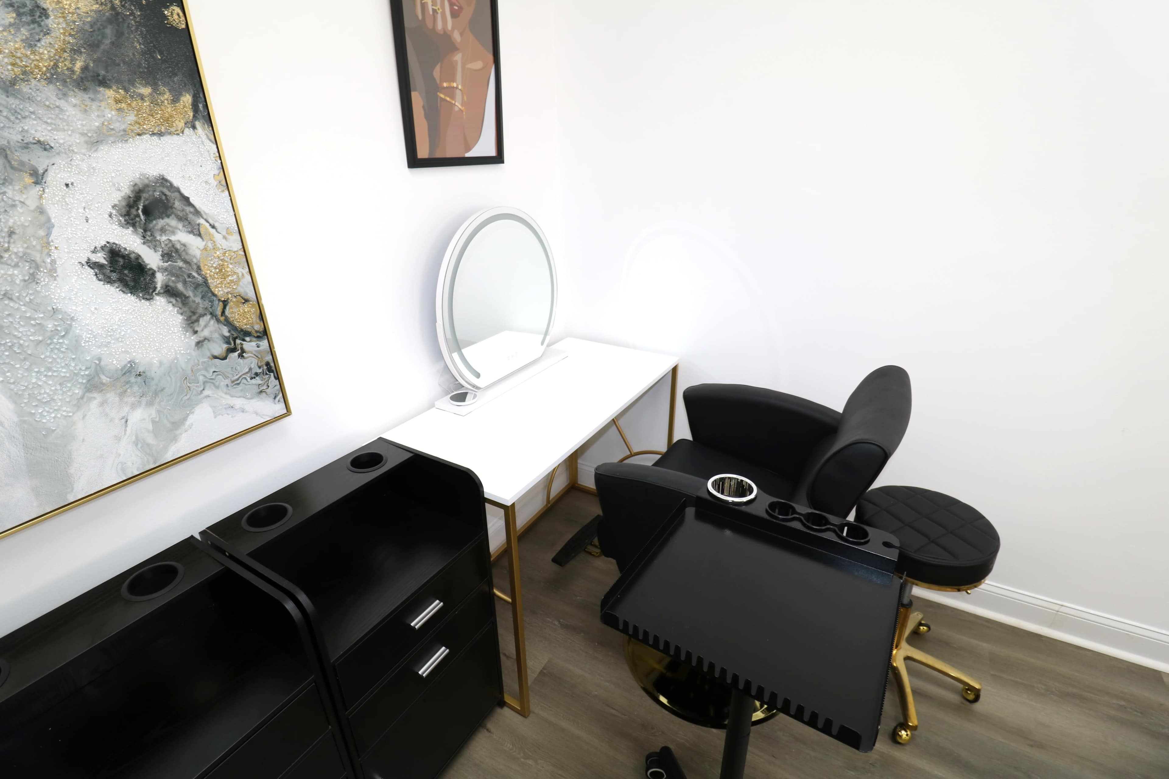 The image shows a minimalist beauty salon interior with a makeup station featuring a round mirror, a black chair, and storage cabinets.