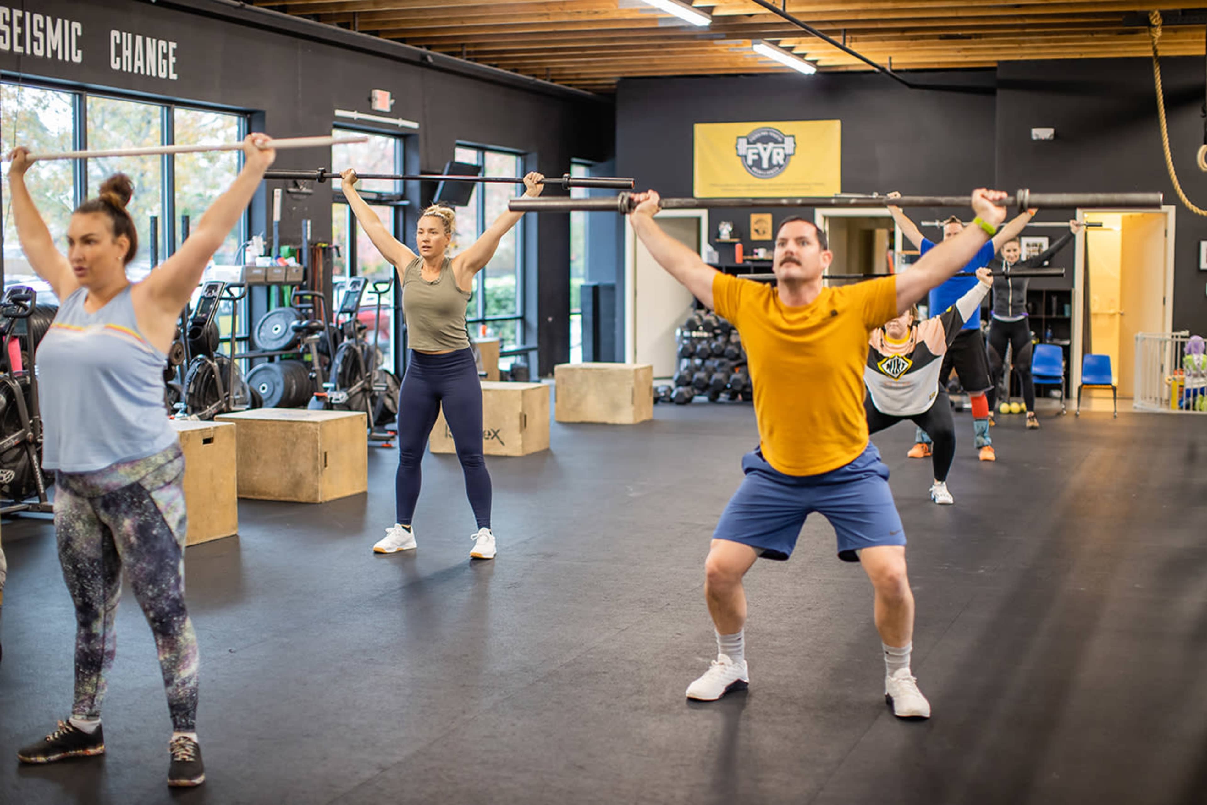 A group of people is participating in a weightlifting workout in a gym setting.