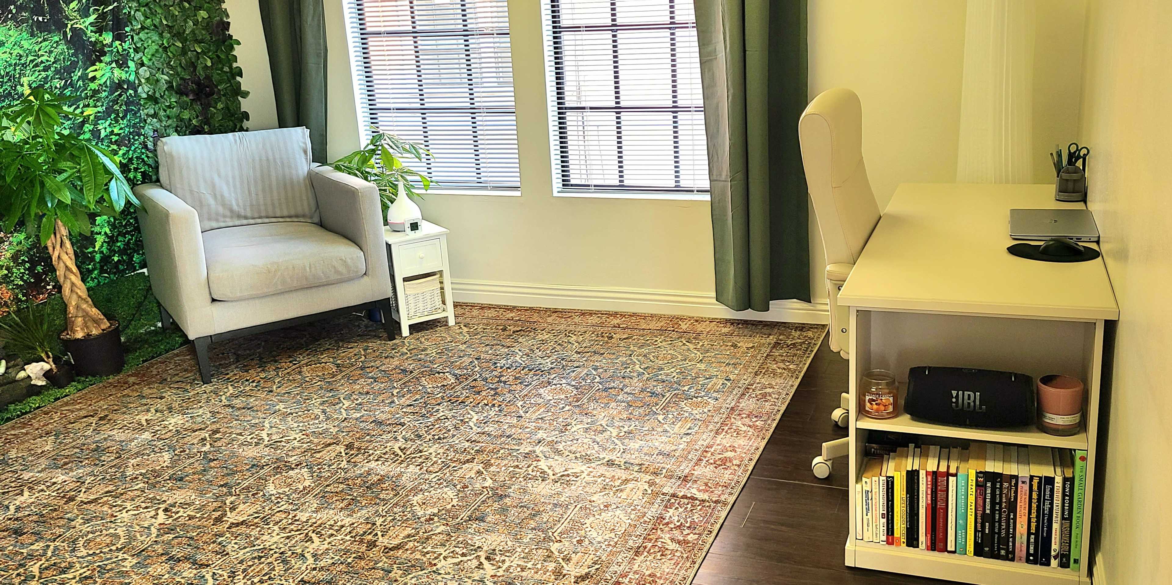 A small, well-lit room with a chair, a desk with books and a speaker, and plants near a wall covered in greenery.