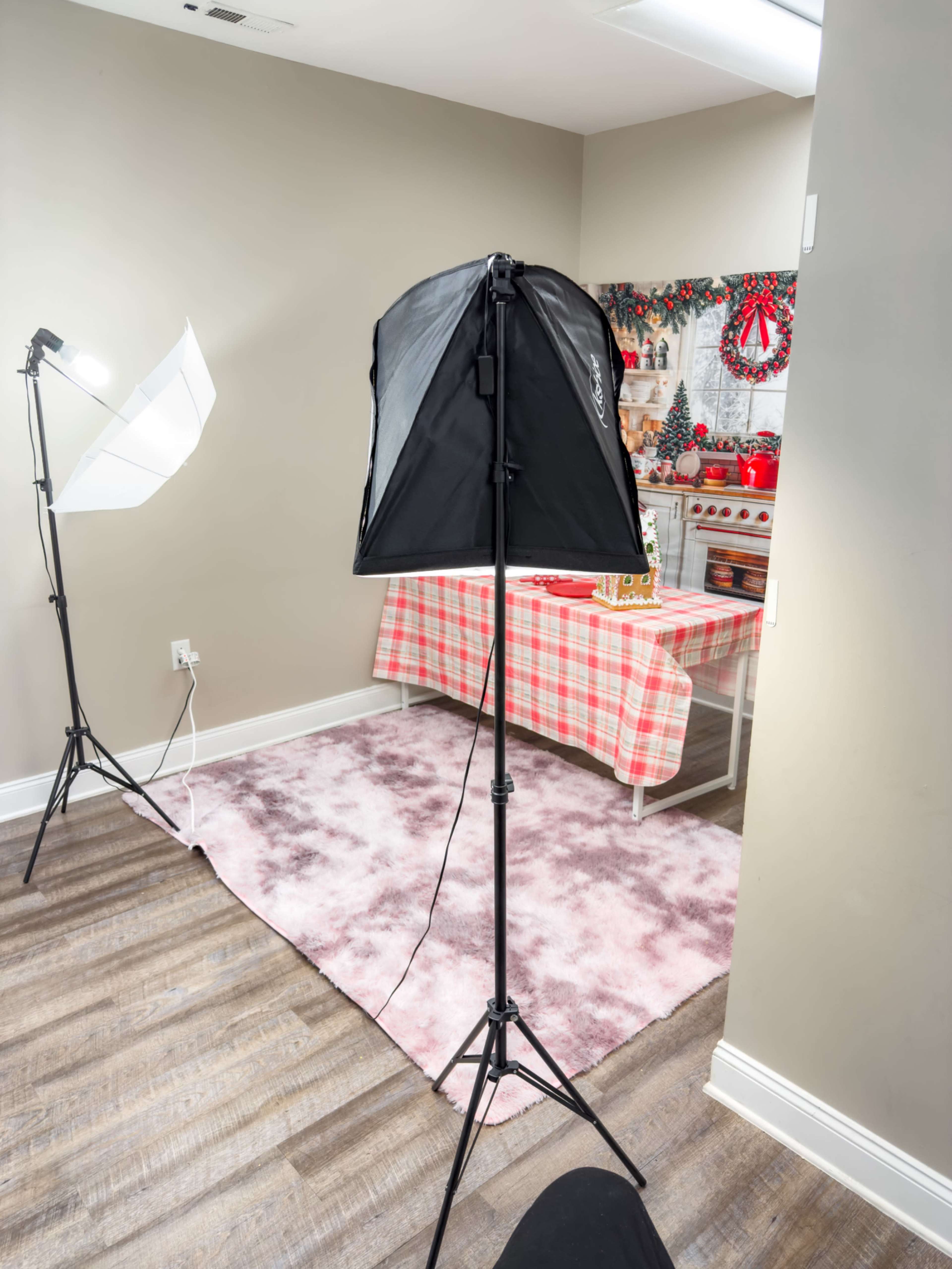 The image shows a well-lit studio setup with a photography light umbrella and a backdrop featuring a festive table setting near a kitchen area.