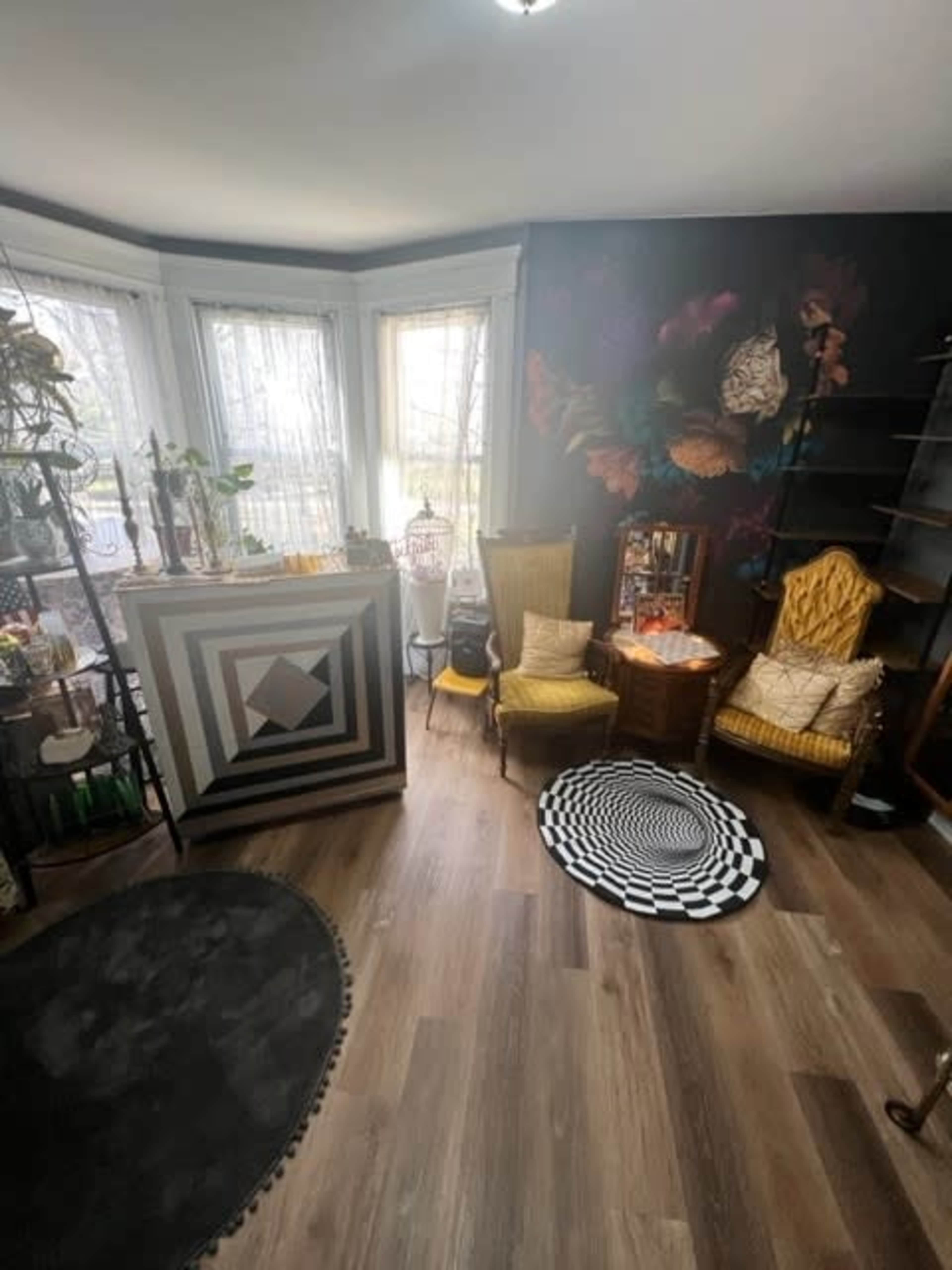 A room with a geometric-patterned bar area, two vintage chairs, a round patterned rug, and large windows allowing natural light.