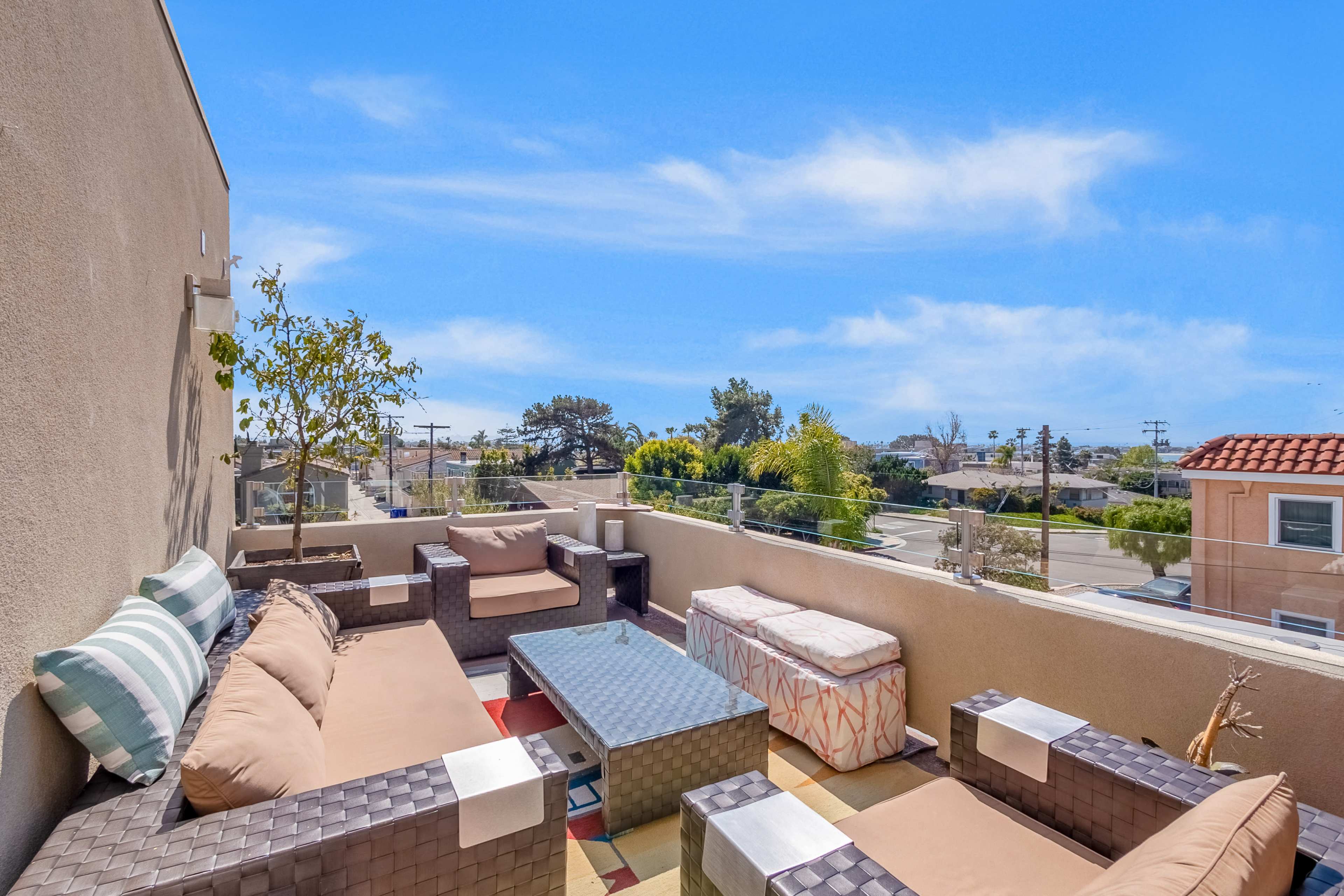 The image shows a rooftop terrace with brown wicker furniture, a glass coffee table, and a clear blue sky above.