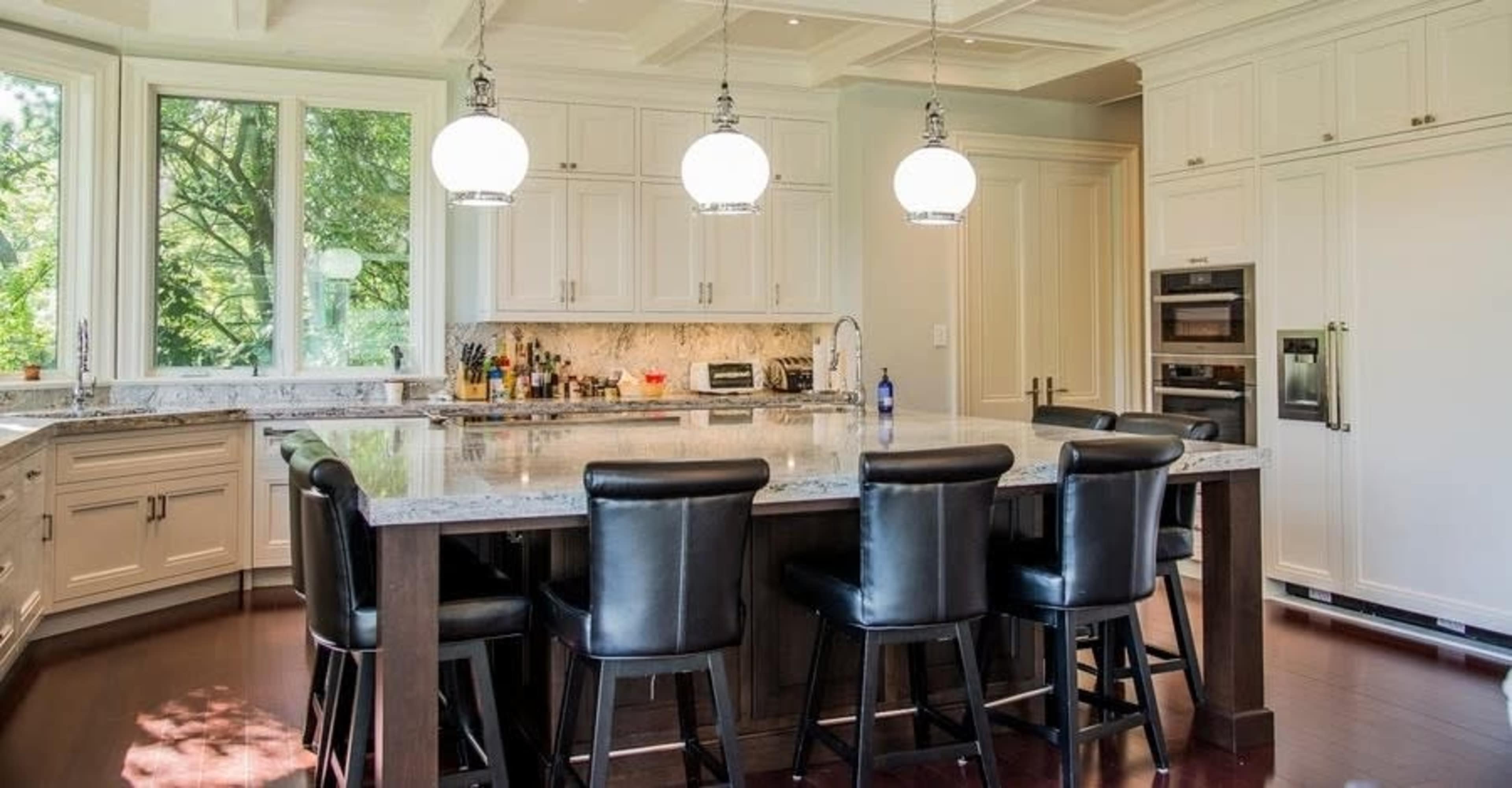 A modern kitchen features a large island with seating, white cabinetry, and pendant lighting above.