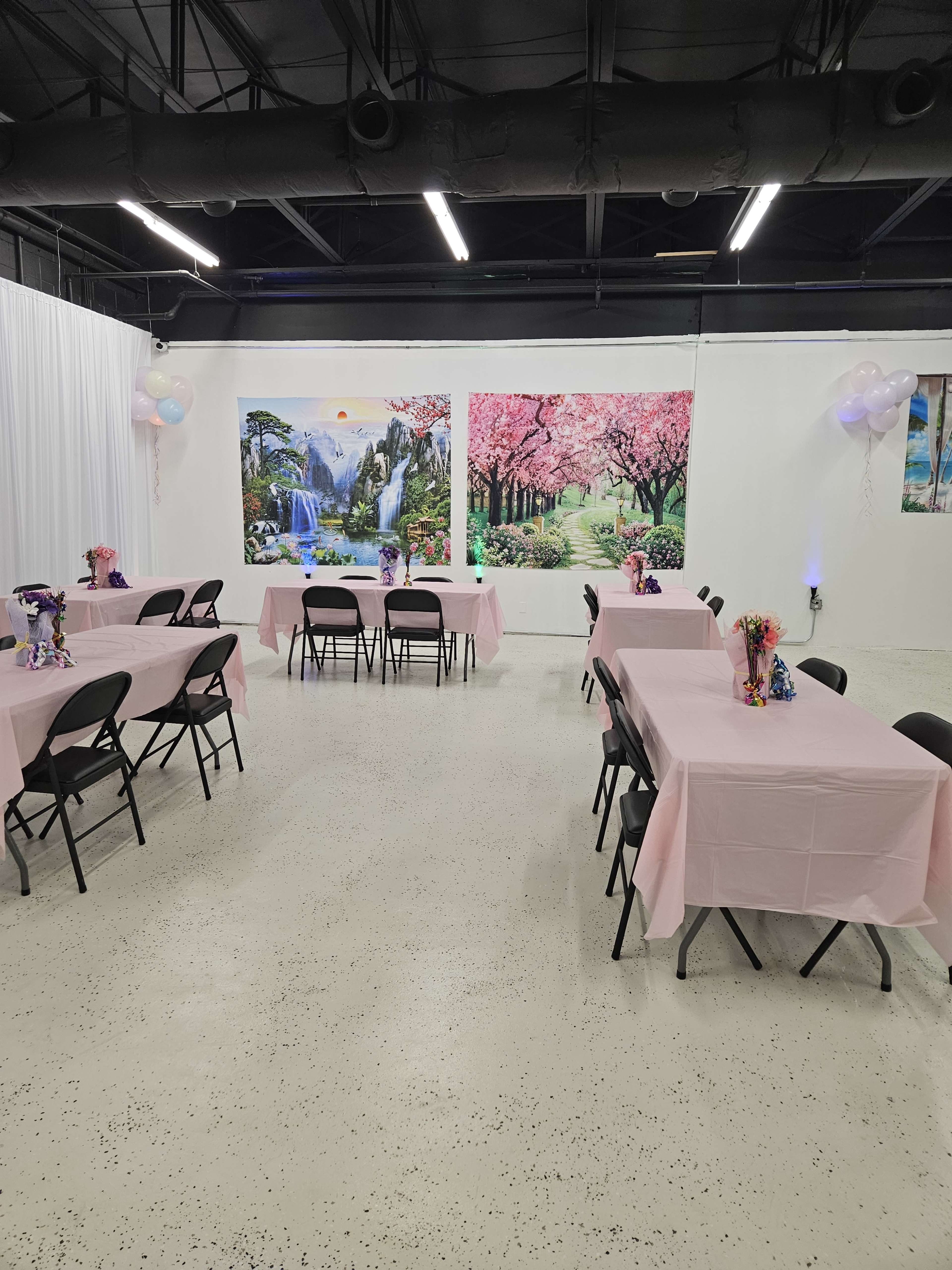 A banquet hall with several tables covered in pink tablecloths, arranged in an open space with floral backdrop decorations on the walls.