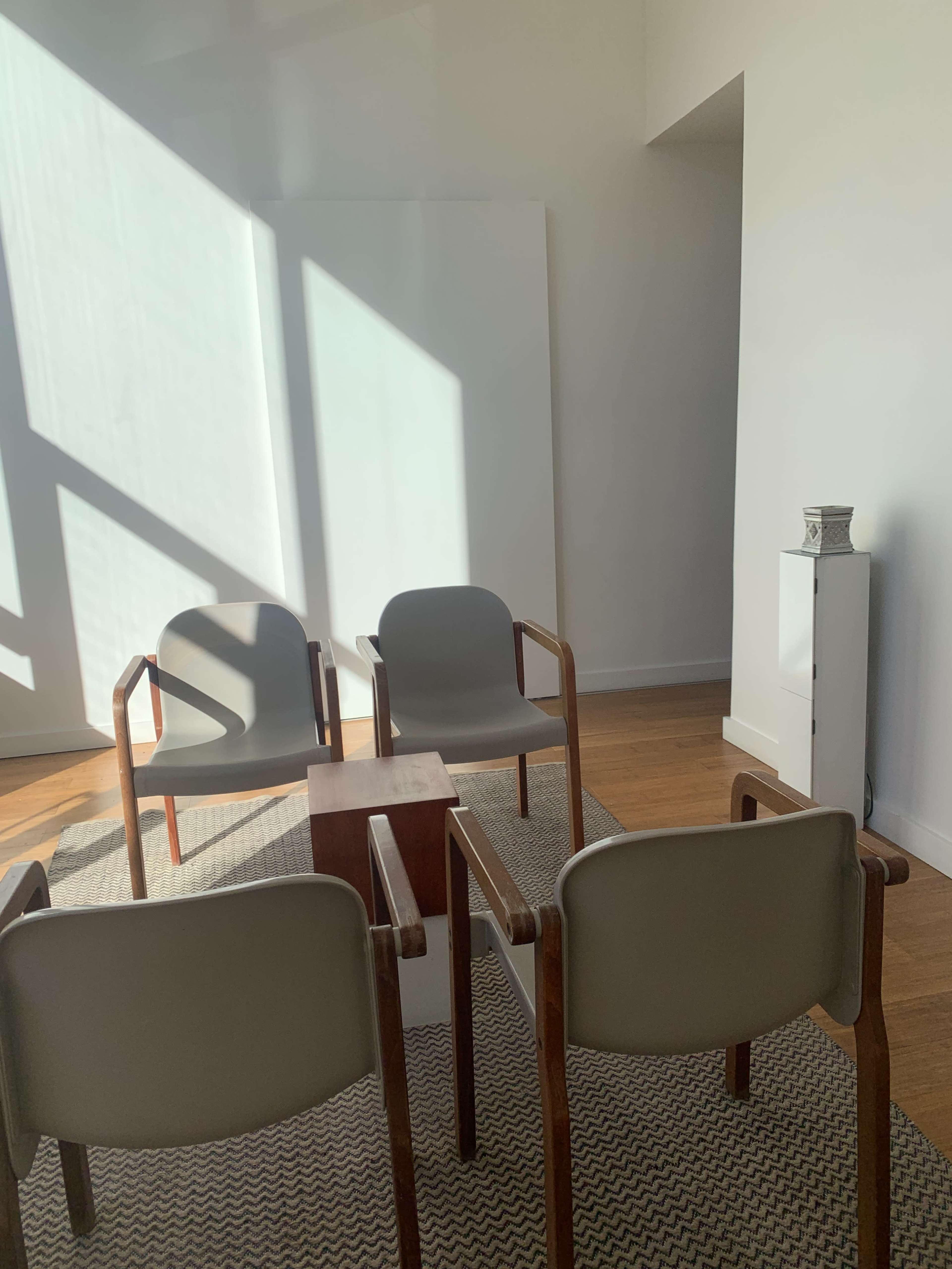 A minimalist room with three chairs arranged around a small wooden table on a patterned rug.