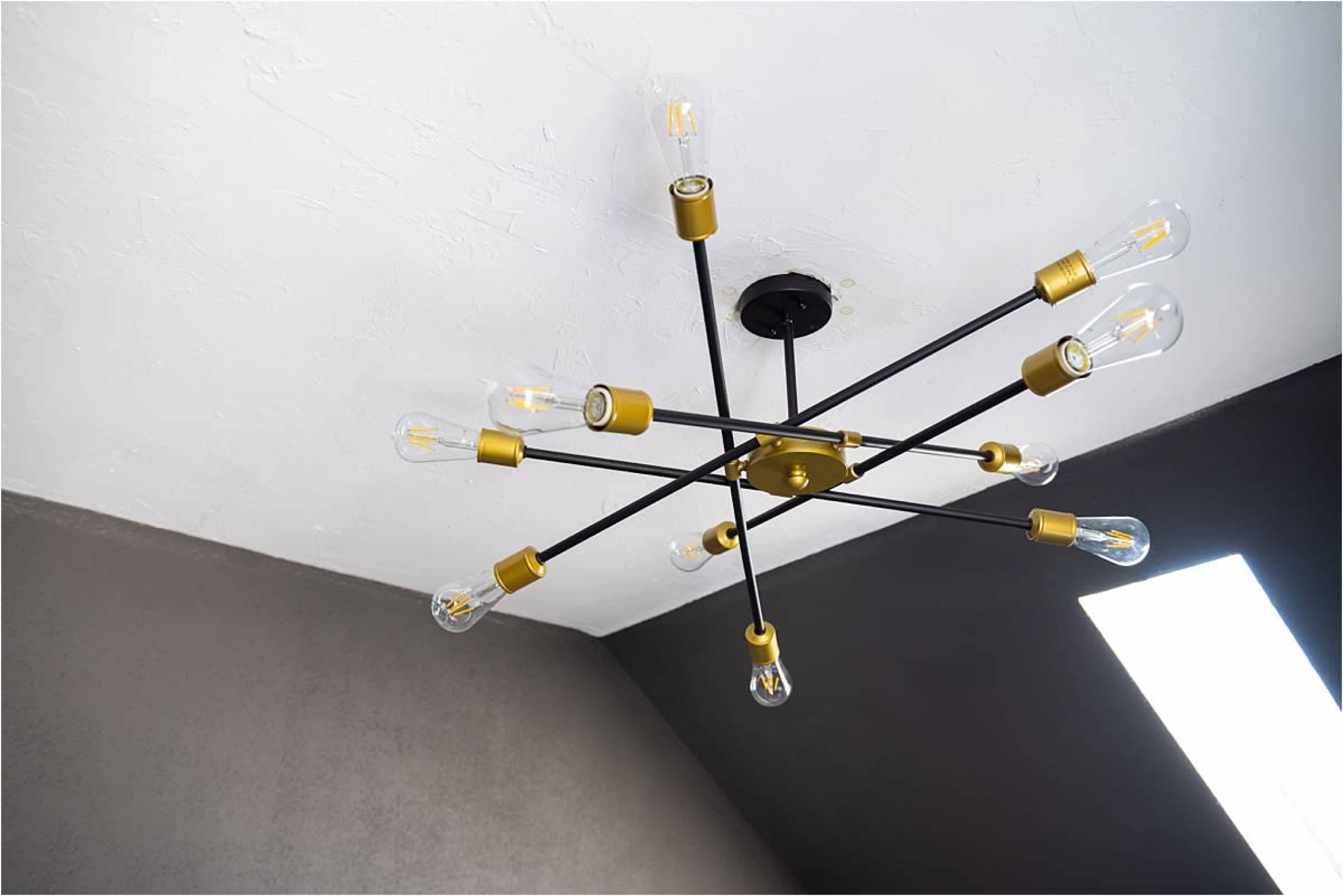 A modern chandelier with multiple light bulbs is mounted on a ceiling, contrasting with the dark wall.