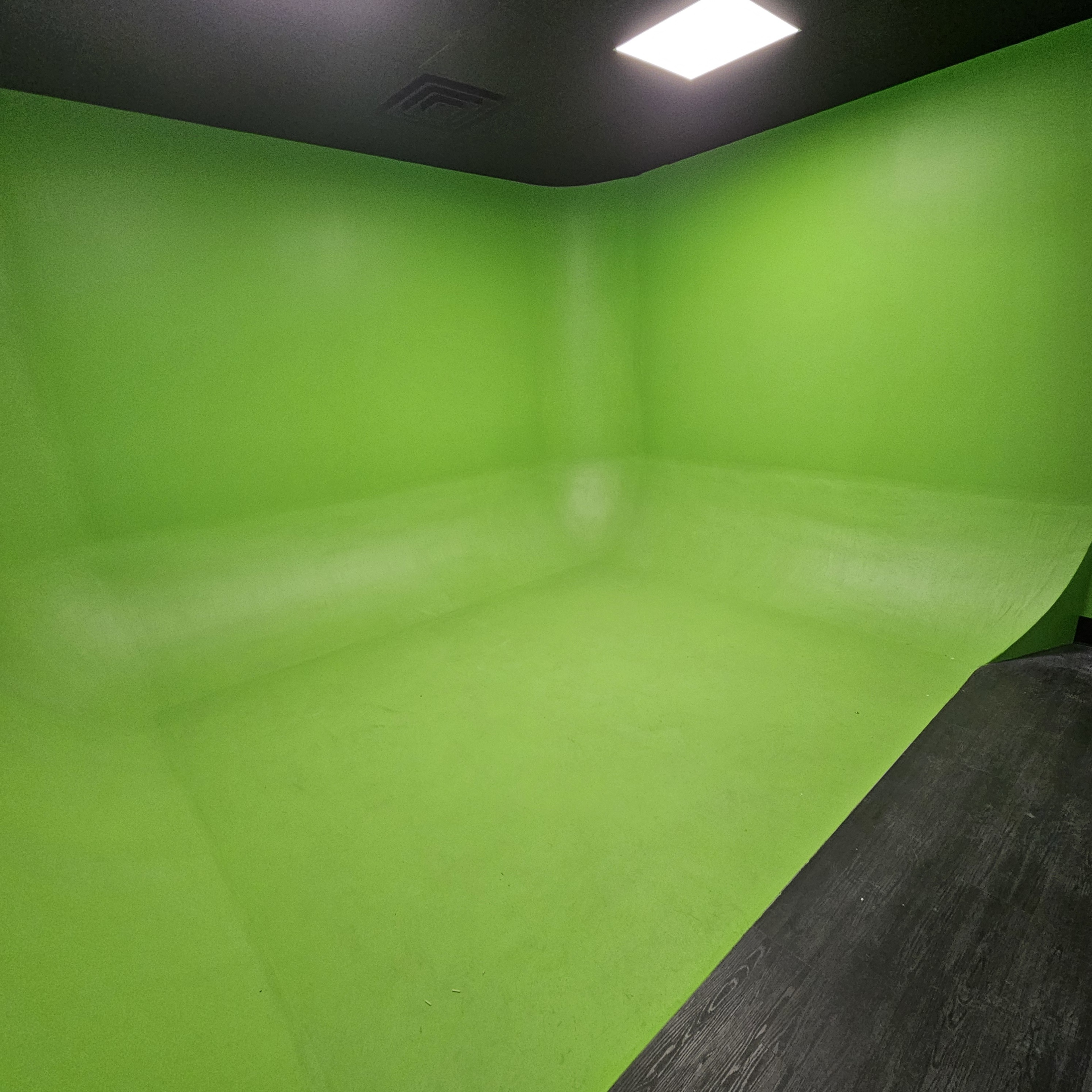 The image shows a room with bright green walls and a curved green floor, commonly used as a green screen backdrop.