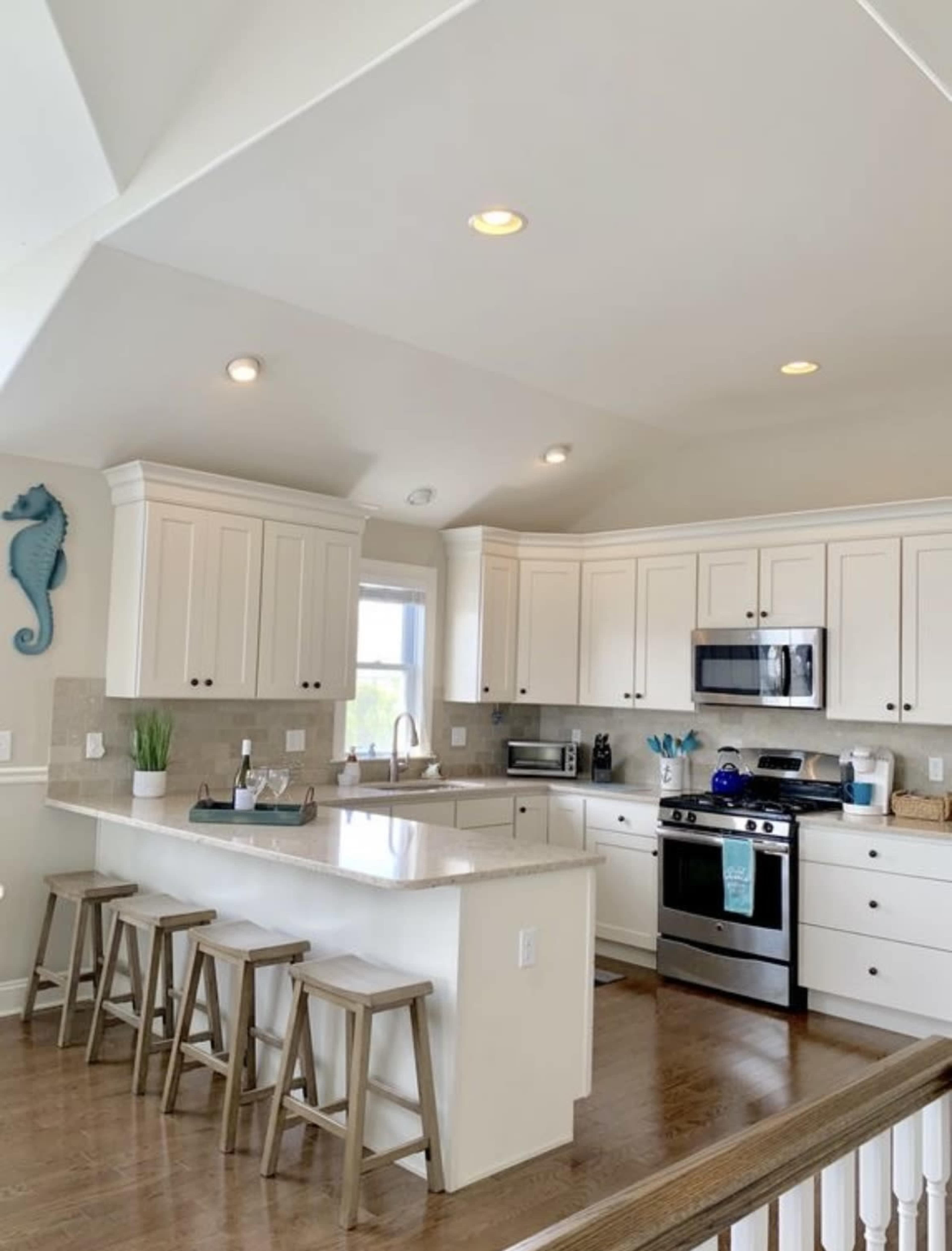 A modern kitchen features white cabinetry, stainless steel appliances, and a central island with seating for three.
