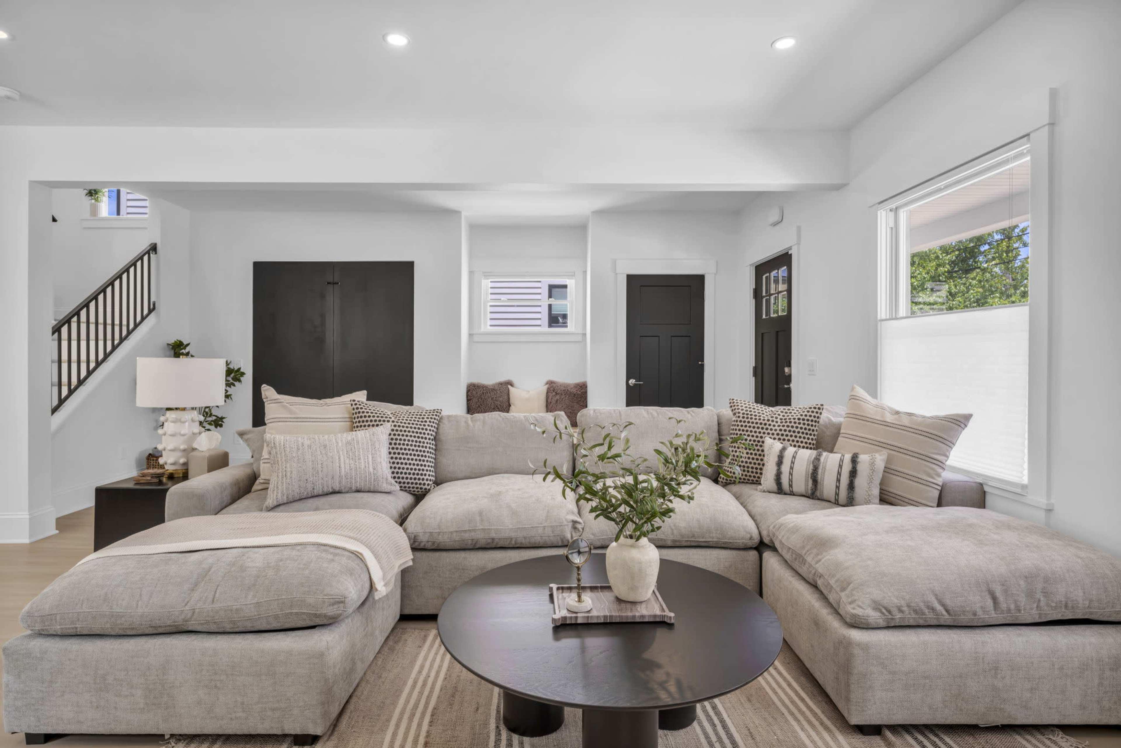 A modern living room features a large sectional sofa, a round coffee table, and decorative elements like a plant and pillows.