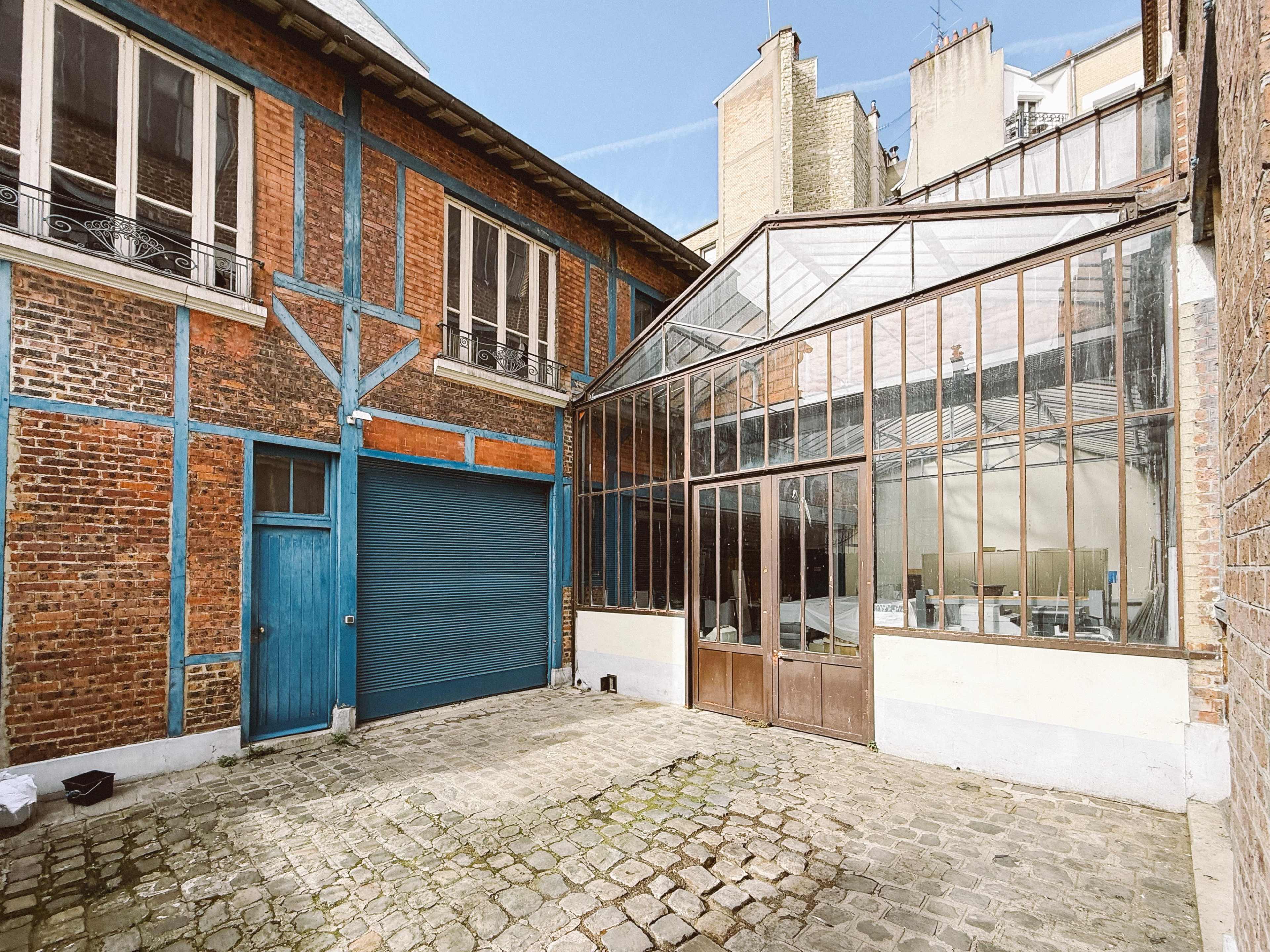 The image shows a courtyard featuring a brick building with blue accents and a glass greenhouse structure.