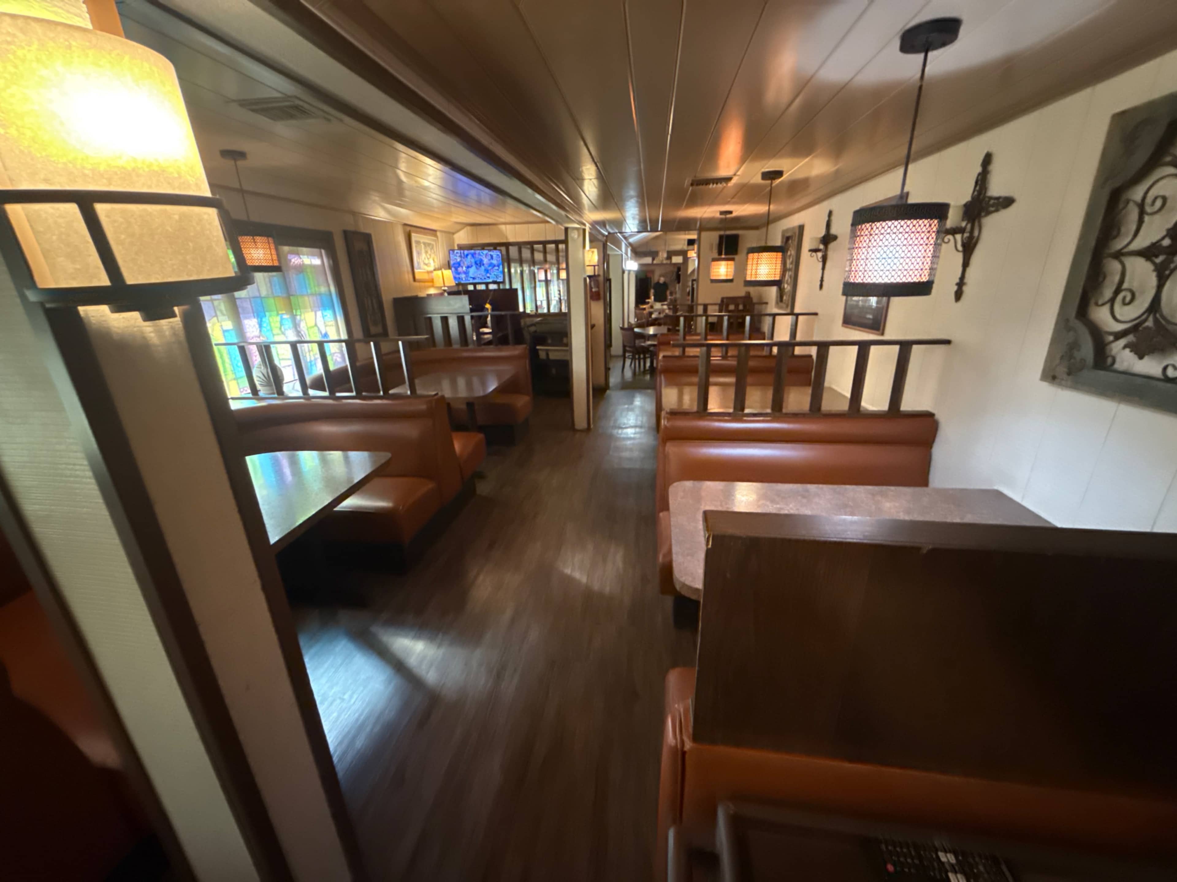 The image shows the interior of a restaurant with wooden booths, a long narrow layout, and decorative lighting.