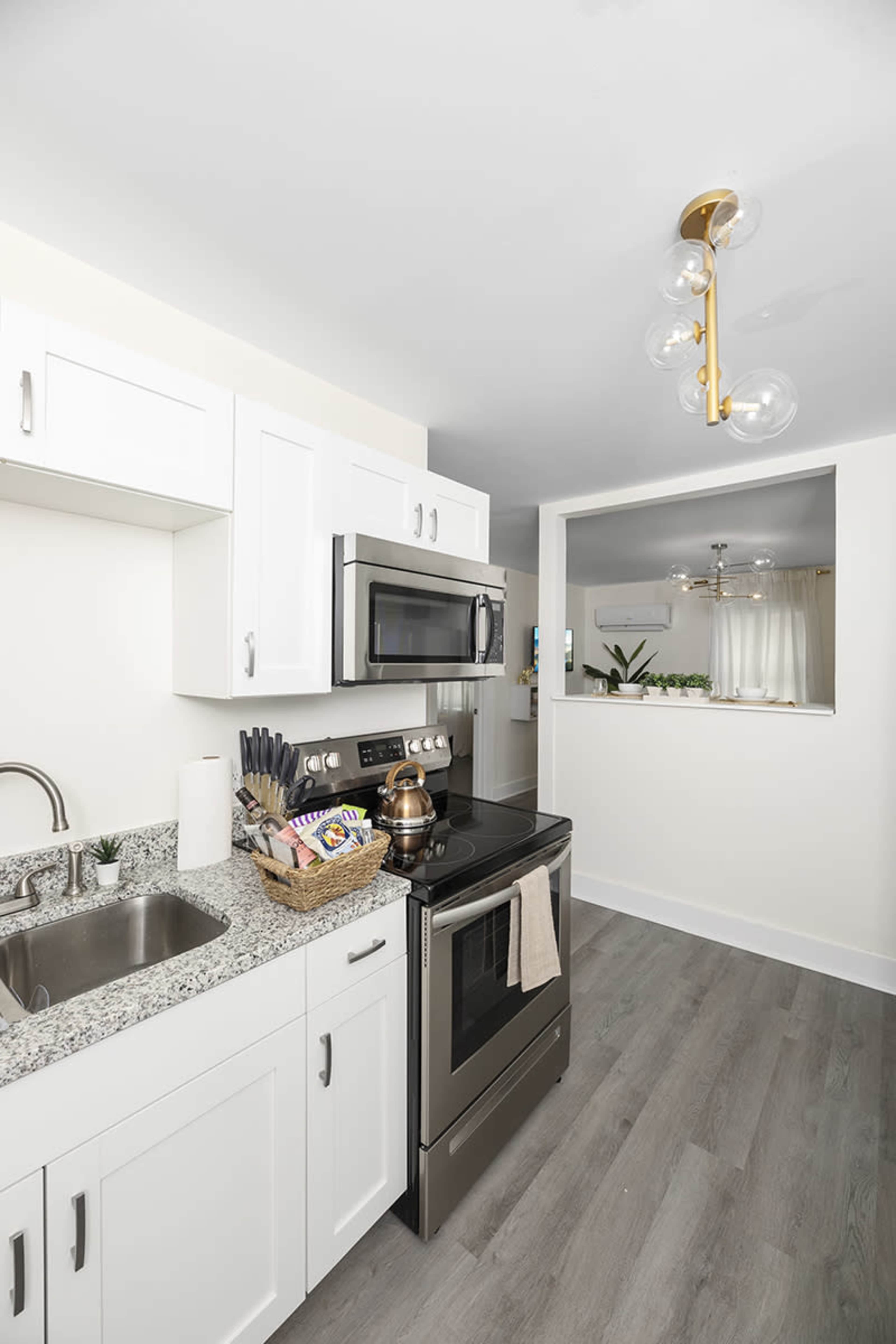 A modern kitchen features white cabinets, a stainless steel microwave and oven, and a granite countertop with a sink and decorative basket.