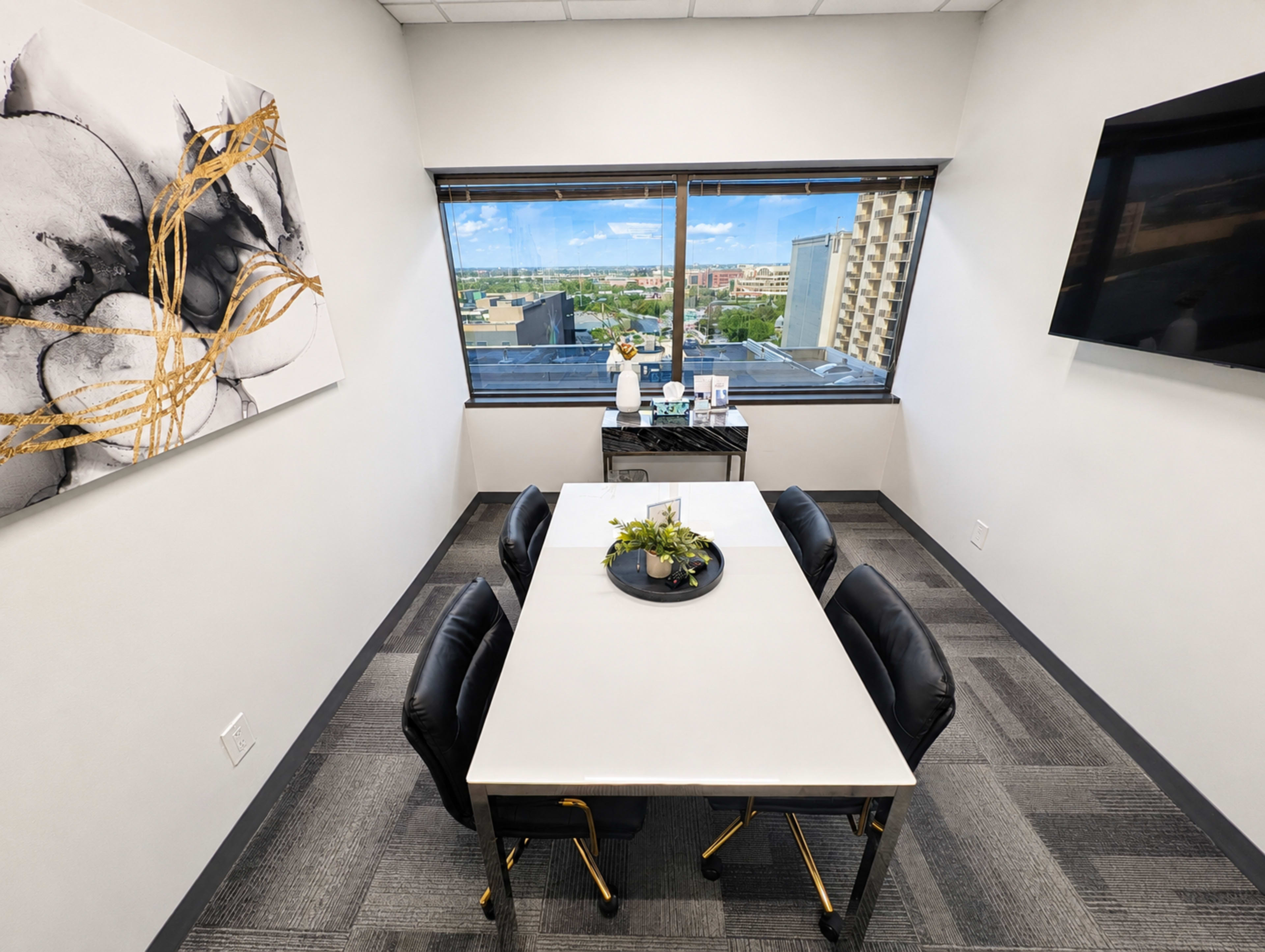 The image shows a modern meeting room with a white table surrounded by black chairs, large windows offering a view of the city, and minimalist decor on the walls.