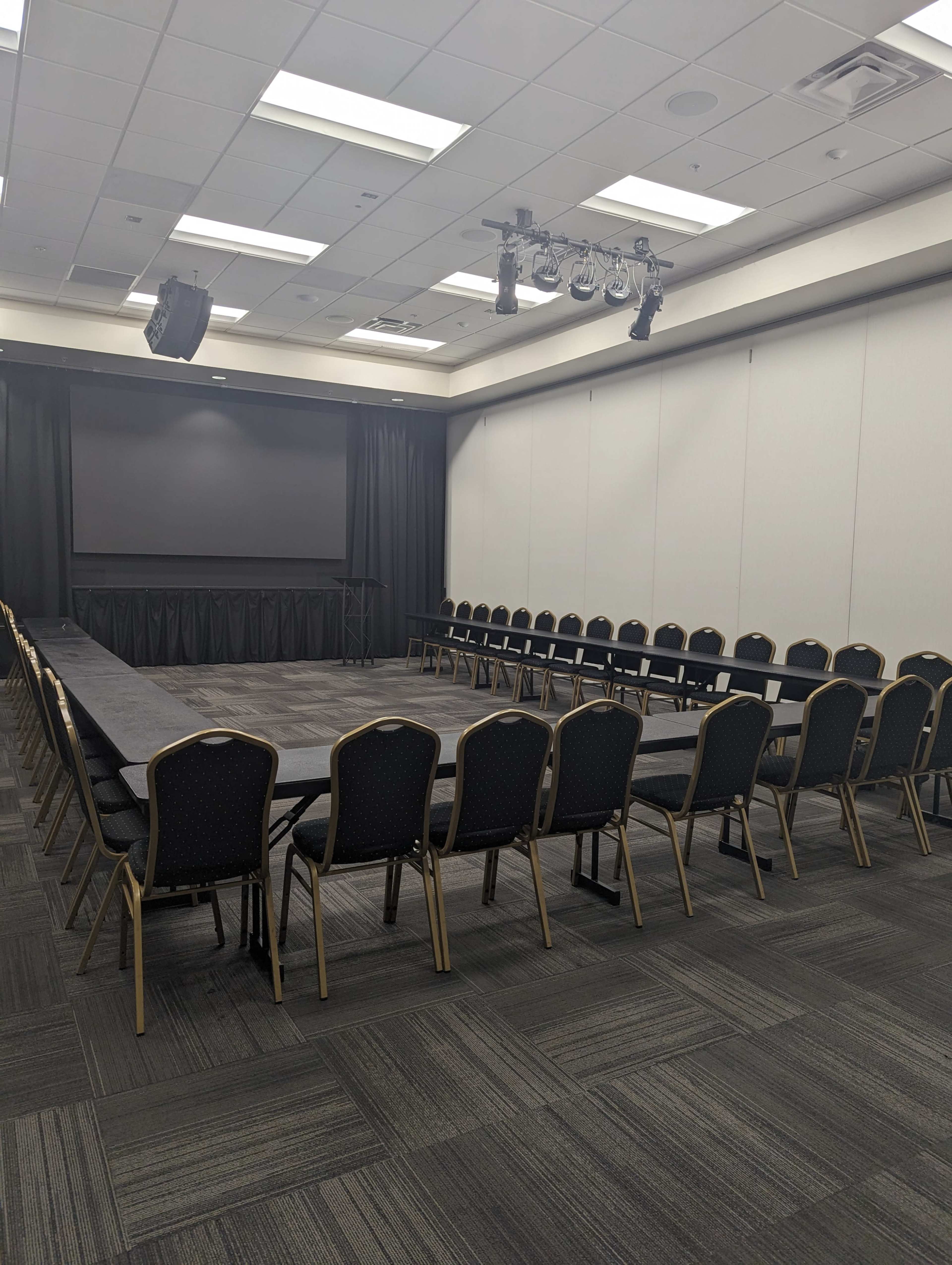 A conference room arranged with a large round table surrounded by chairs, facing a screen at the front.