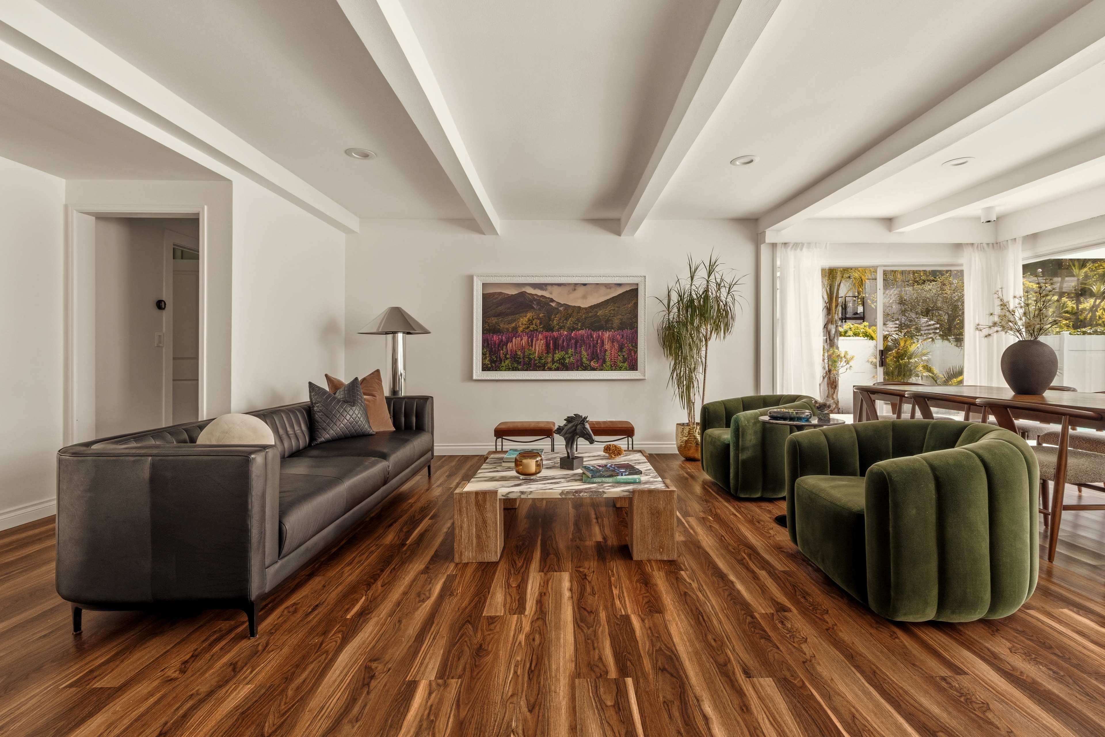 The living room features a black leather sofa, two green chairs, a wooden coffee table, and a large artwork on the wall.