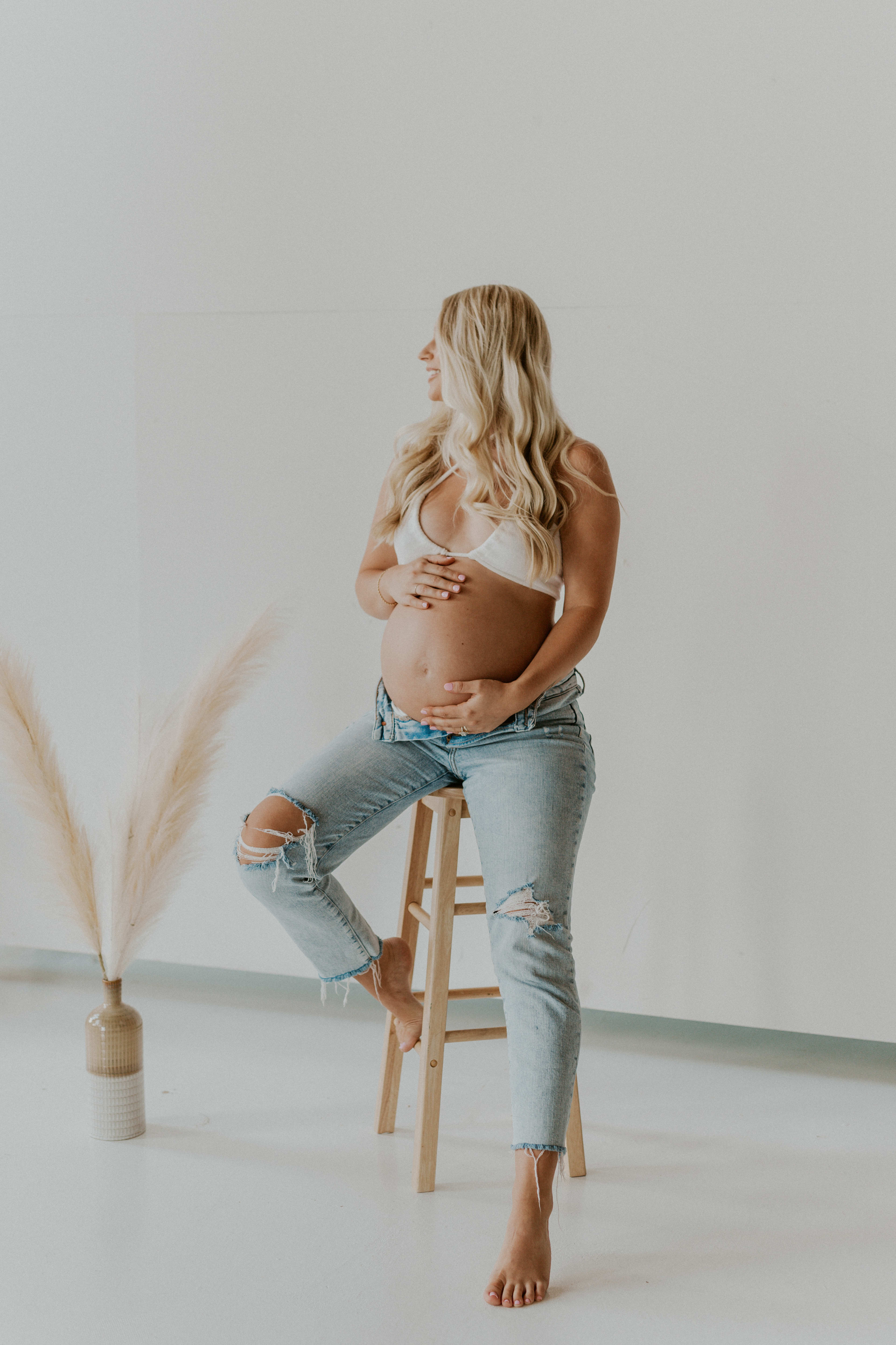 A pregnant woman is sitting on a stool.