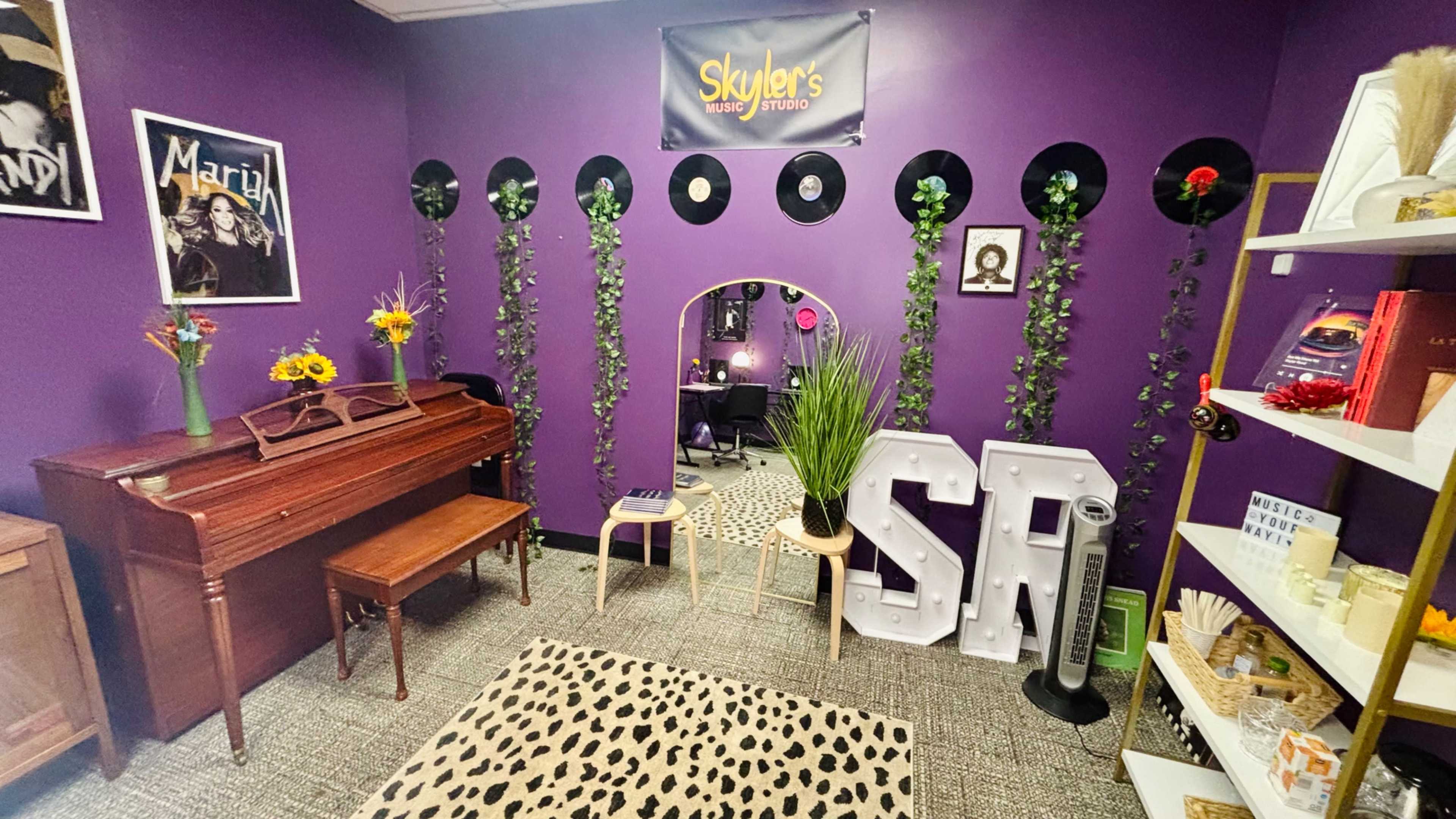 The image shows a vibrant room with purple walls, featuring a piano, decorative vinyl records, a leopard print rug, and various items on shelves.