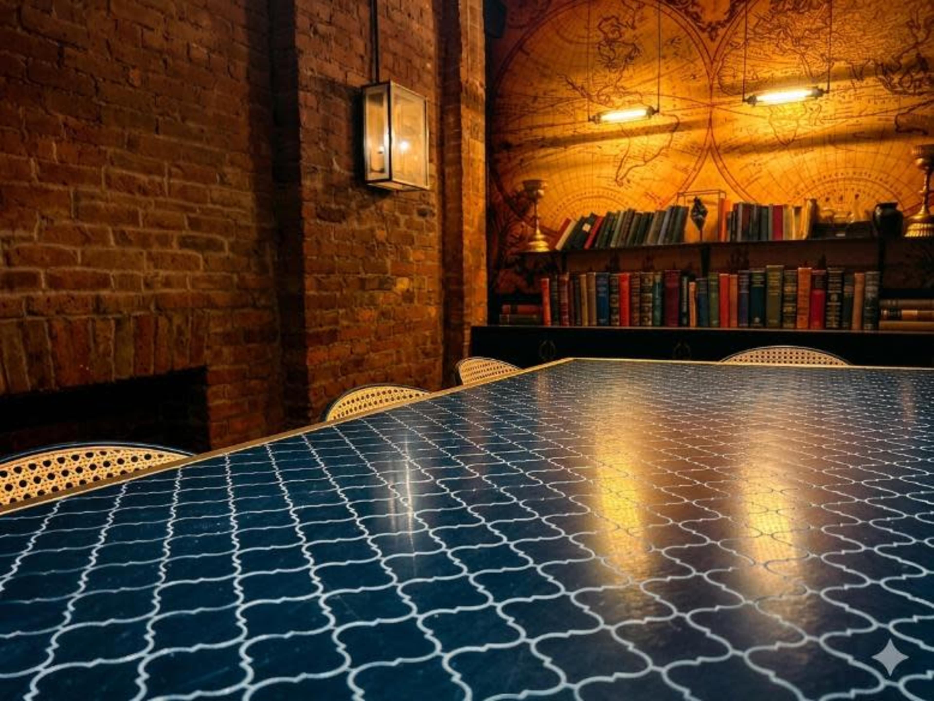 A large, dark blue table with a patterned surface is set against a brick wall and a bookshelf filled with books.