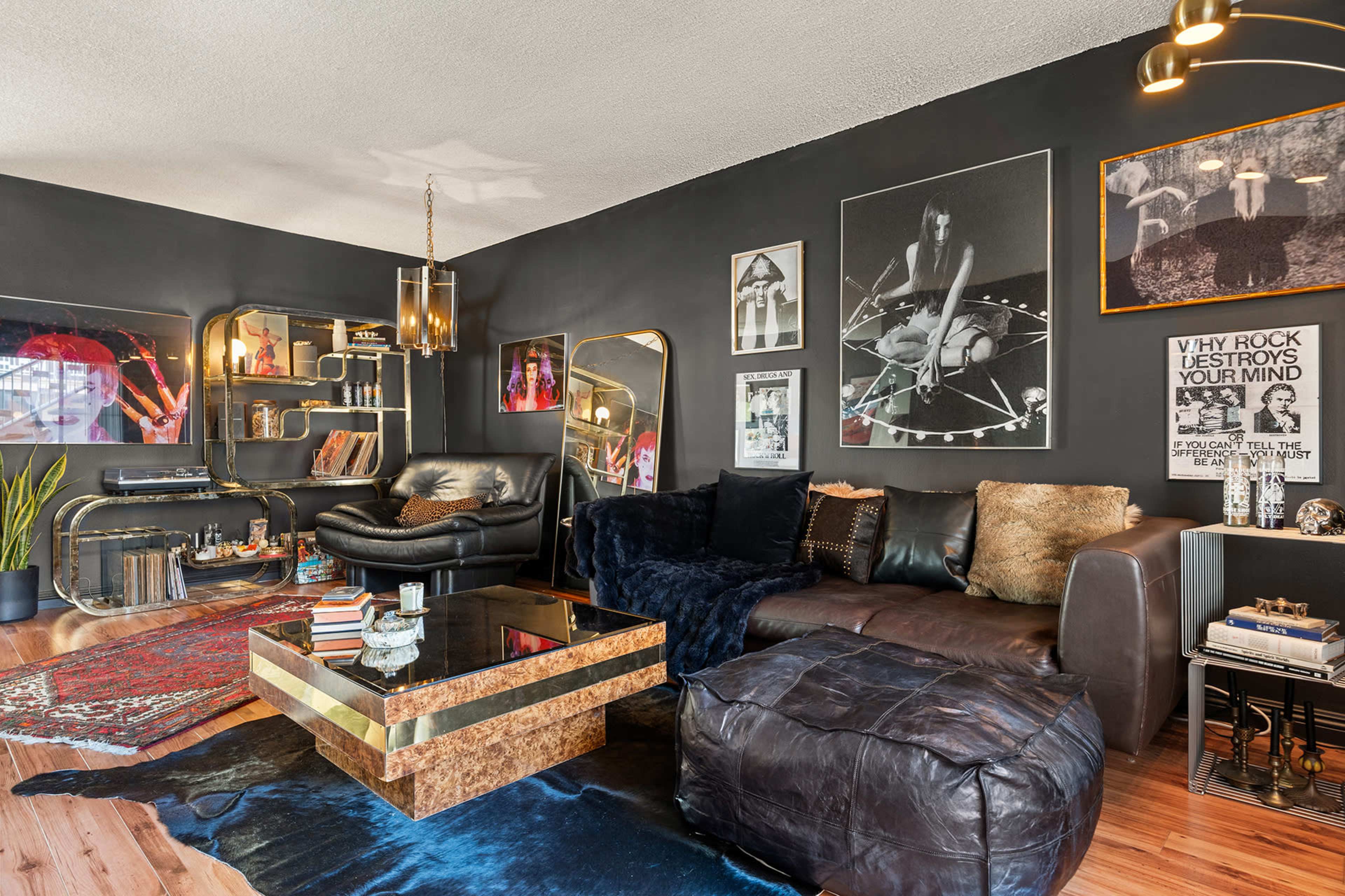 The image showcases a stylish living room featuring a dark wall with various framed artworks, a large sectional sofa, a coffee table, and plush furnishings, all arranged on wooden flooring.