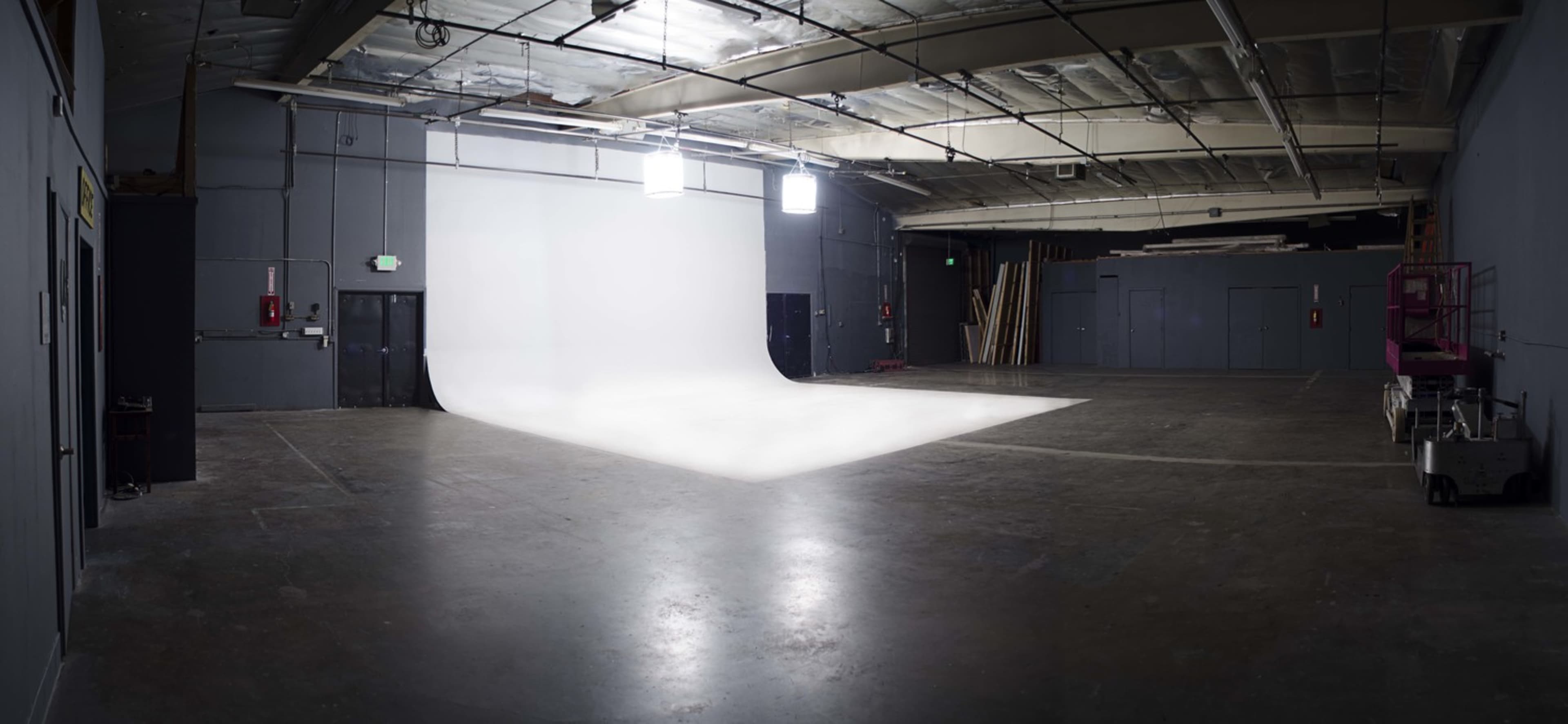 A spacious photo studio with a seamless white backdrop, concrete floors, and overhead lighting.