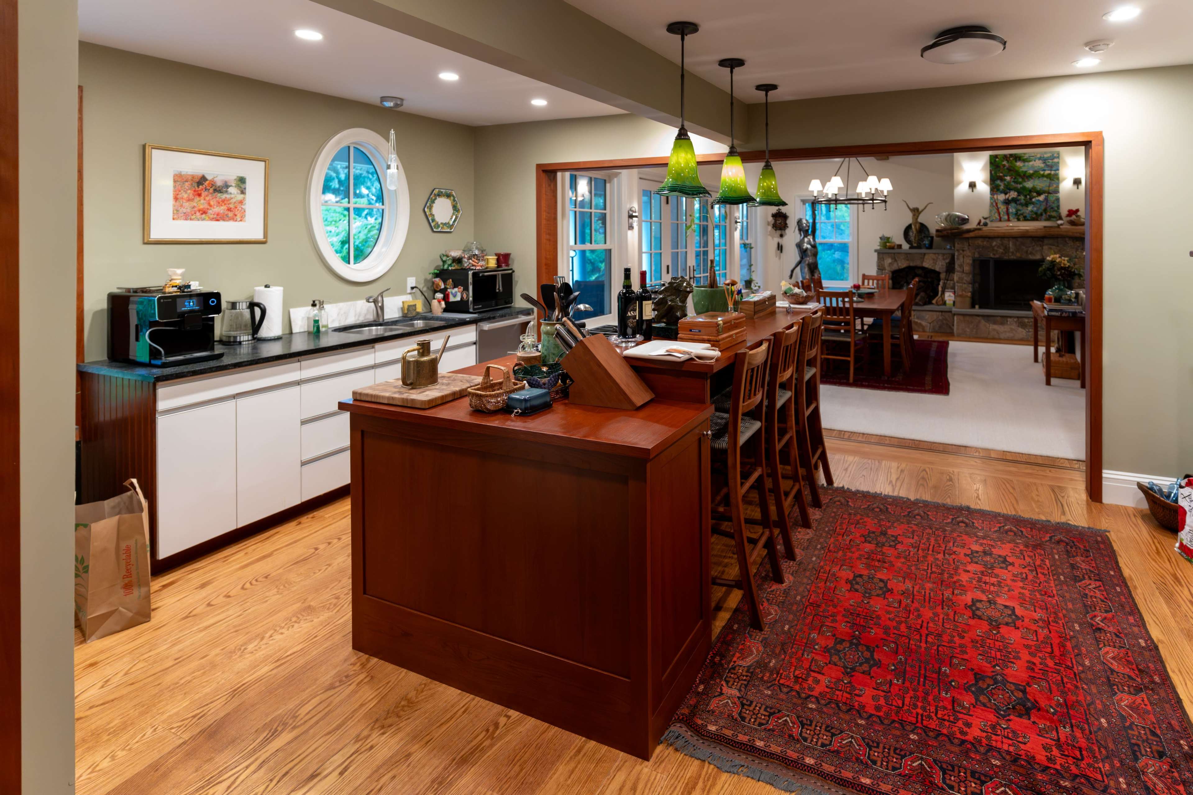 The image shows a modern kitchen featuring a wooden island, barstools, and an adjacent dining area, all set in a well-lit space with decorative elements.