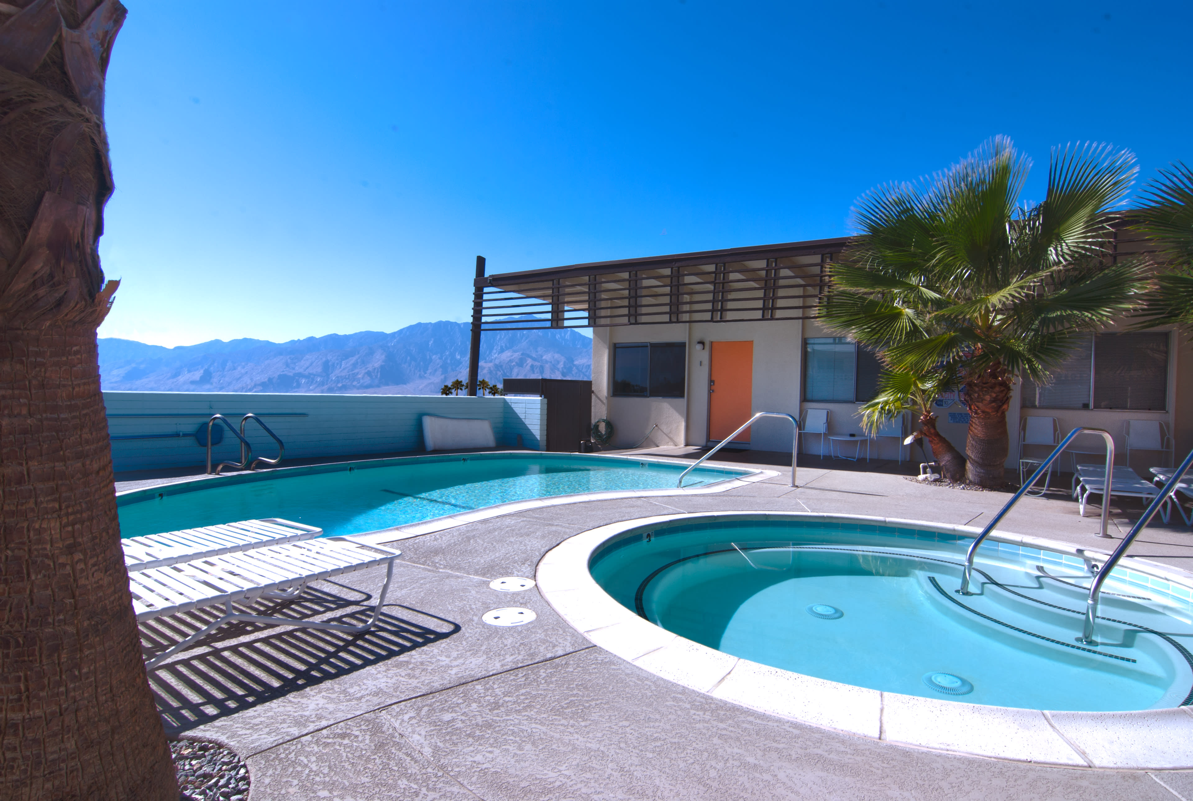 A rooftop pool area features a swimming pool, a hot tub, lounge chairs, and views of the mountains in the background.