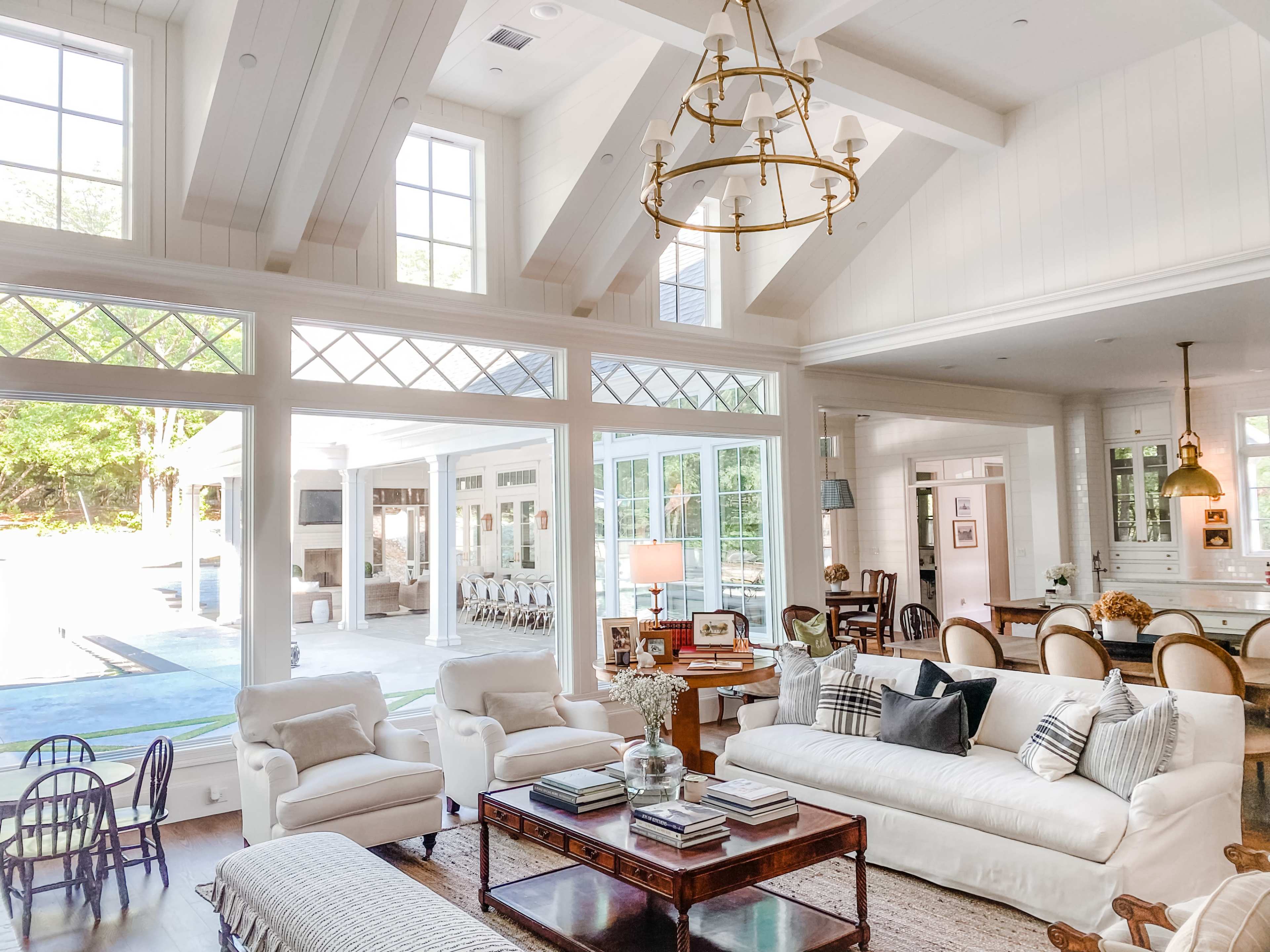 A bright, airy living room with white sofas, a wooden coffee table, and large windows that open to a patio and dining area.