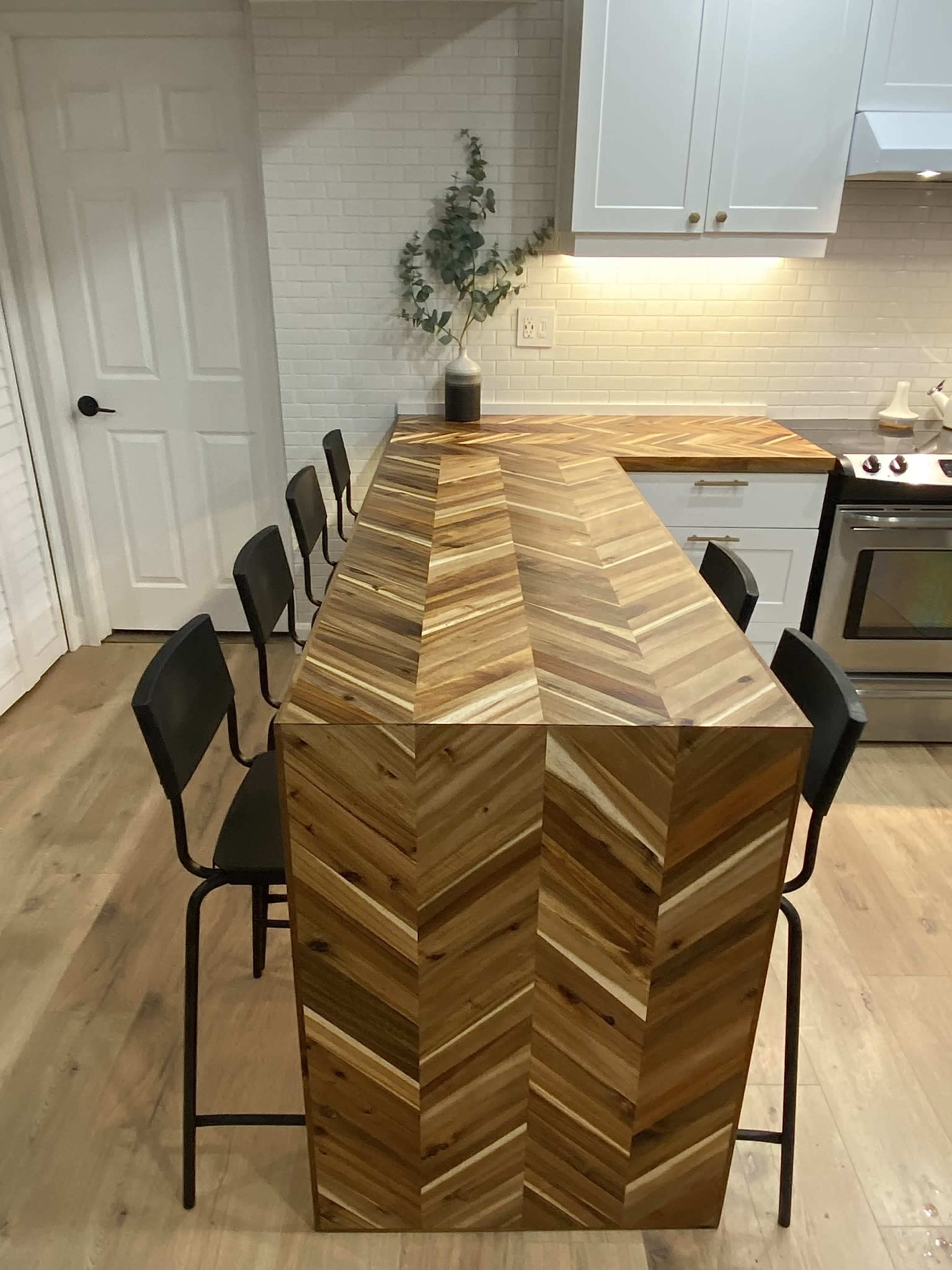 A kitchen features a wooden chevron-patterned island with four black chairs arranged around it.