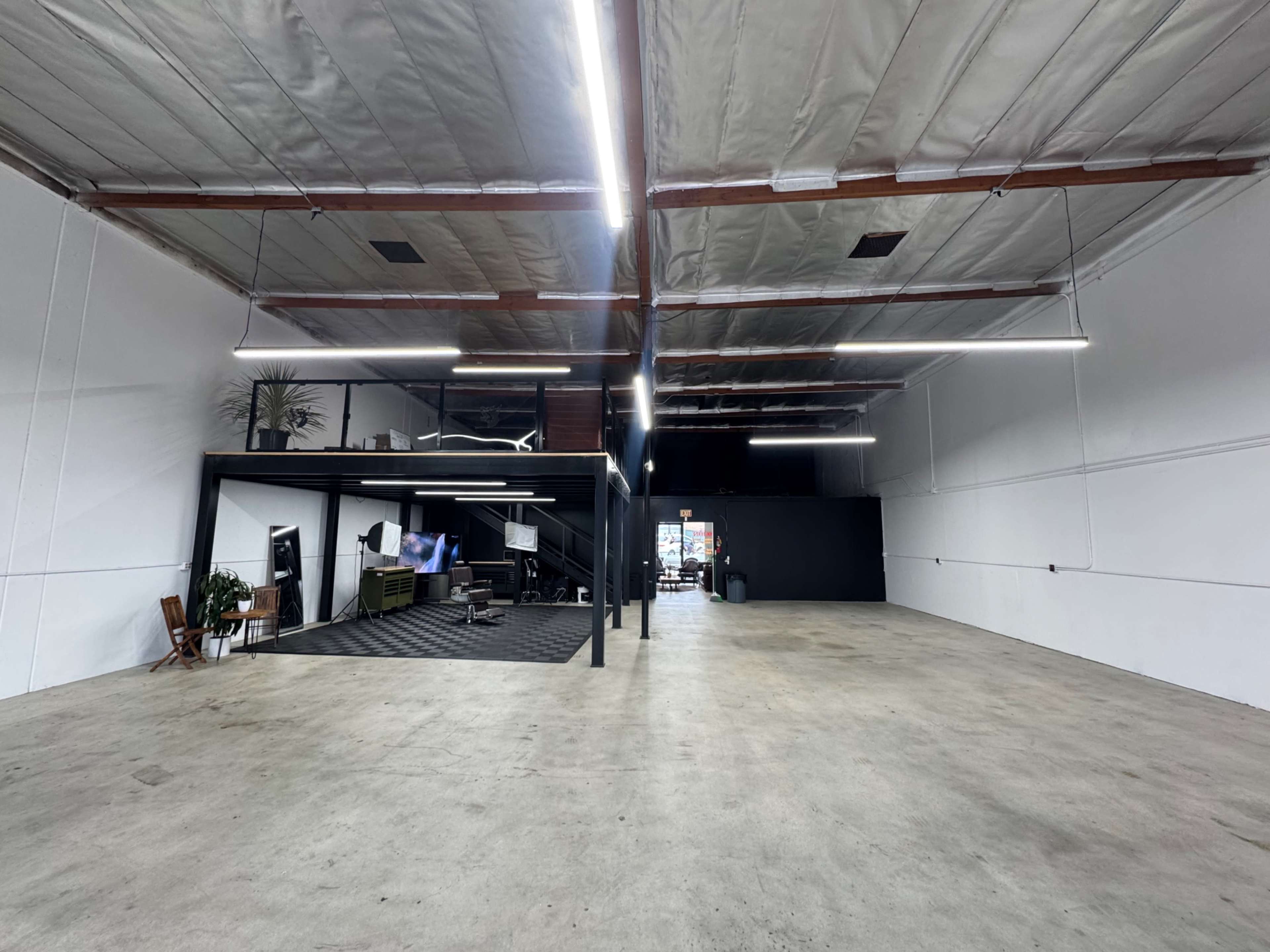 The image shows a spacious, modern industrial warehouse with a black section containing an office area at the far end.