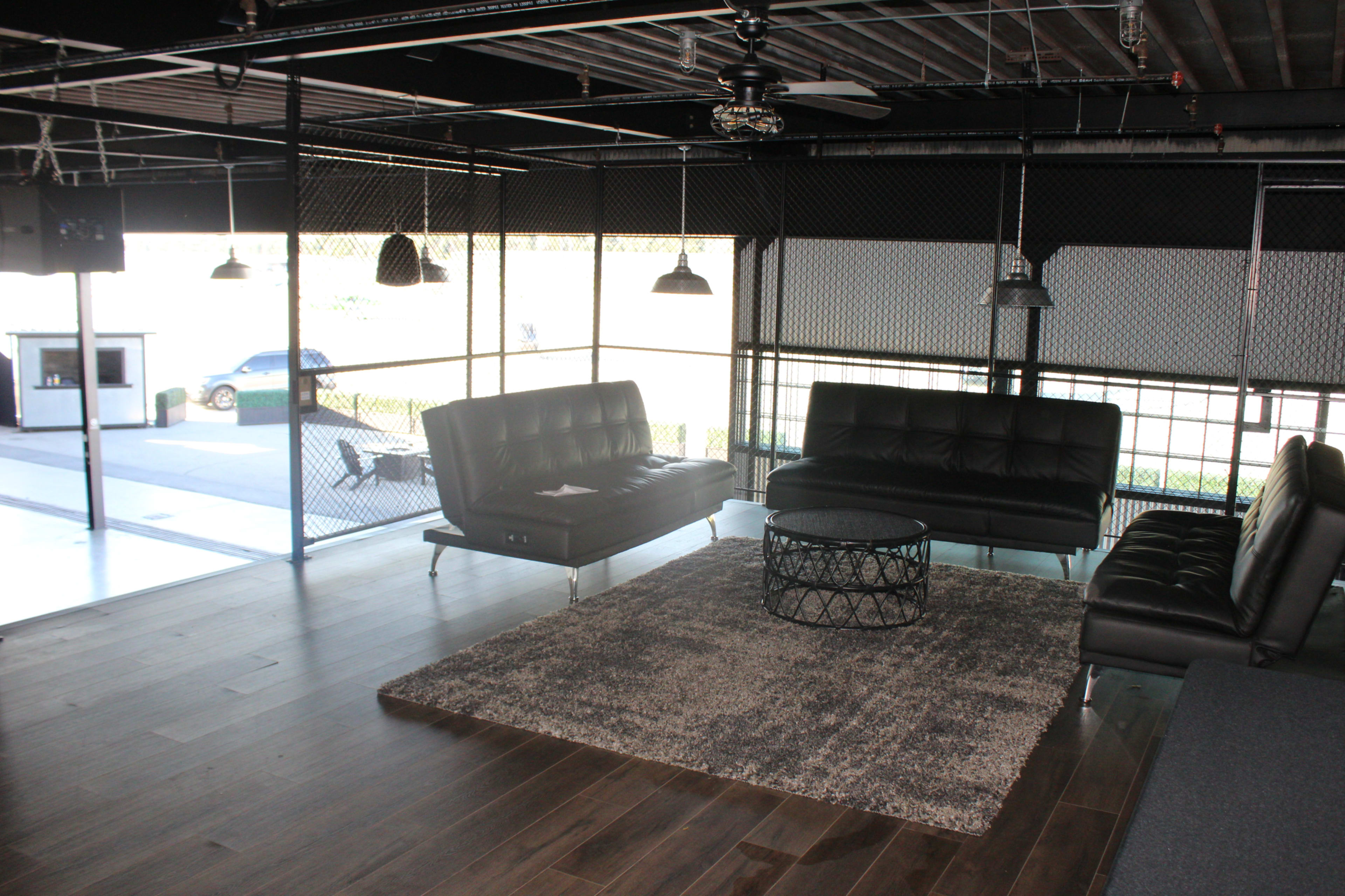 A modern interior lounge area with black sofas, a circular coffee table, and large windows allowing natural light to enter.