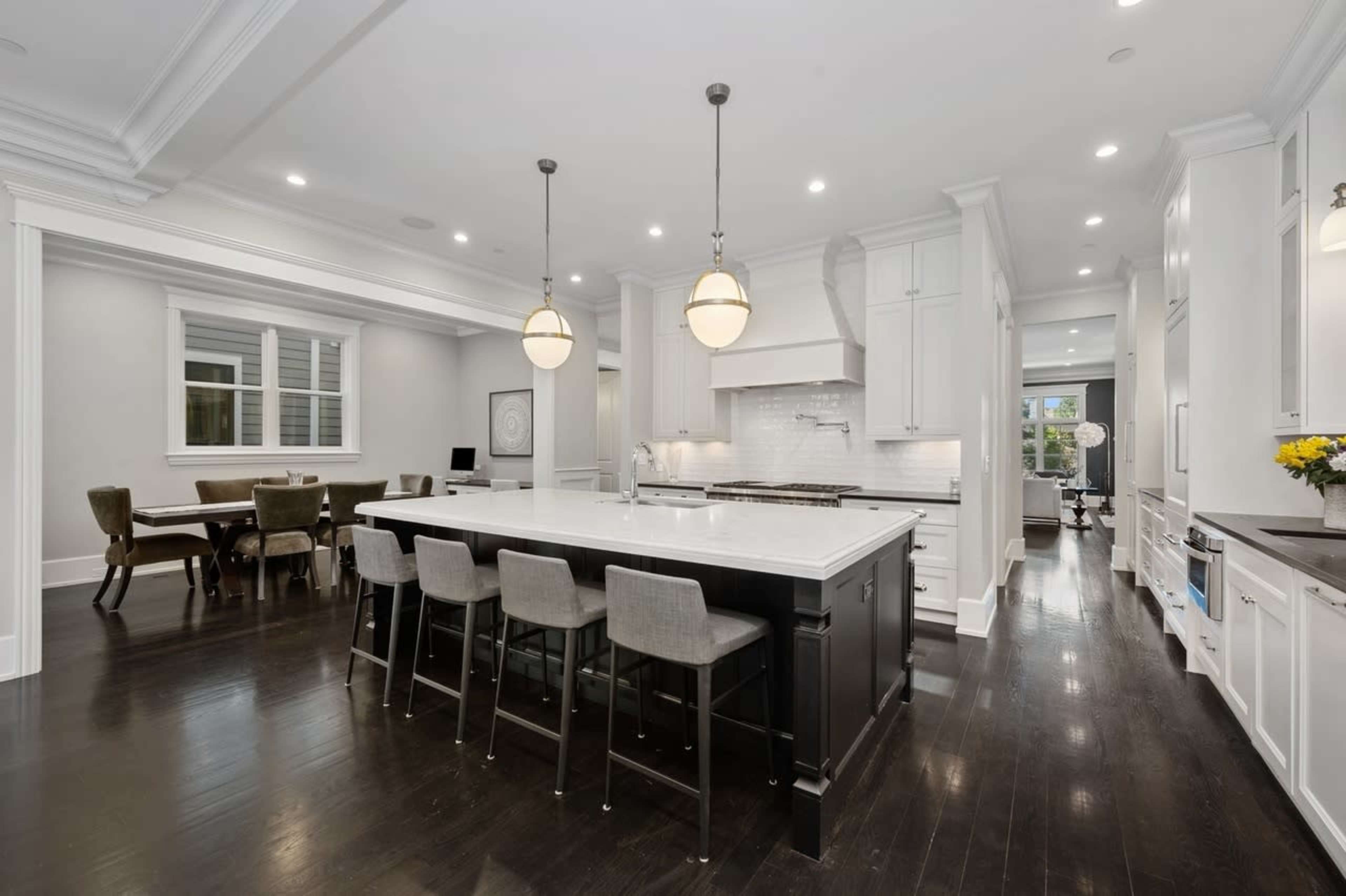 A modern kitchen featuring a large central island with seating, white cabinetry, and dark wooden flooring.