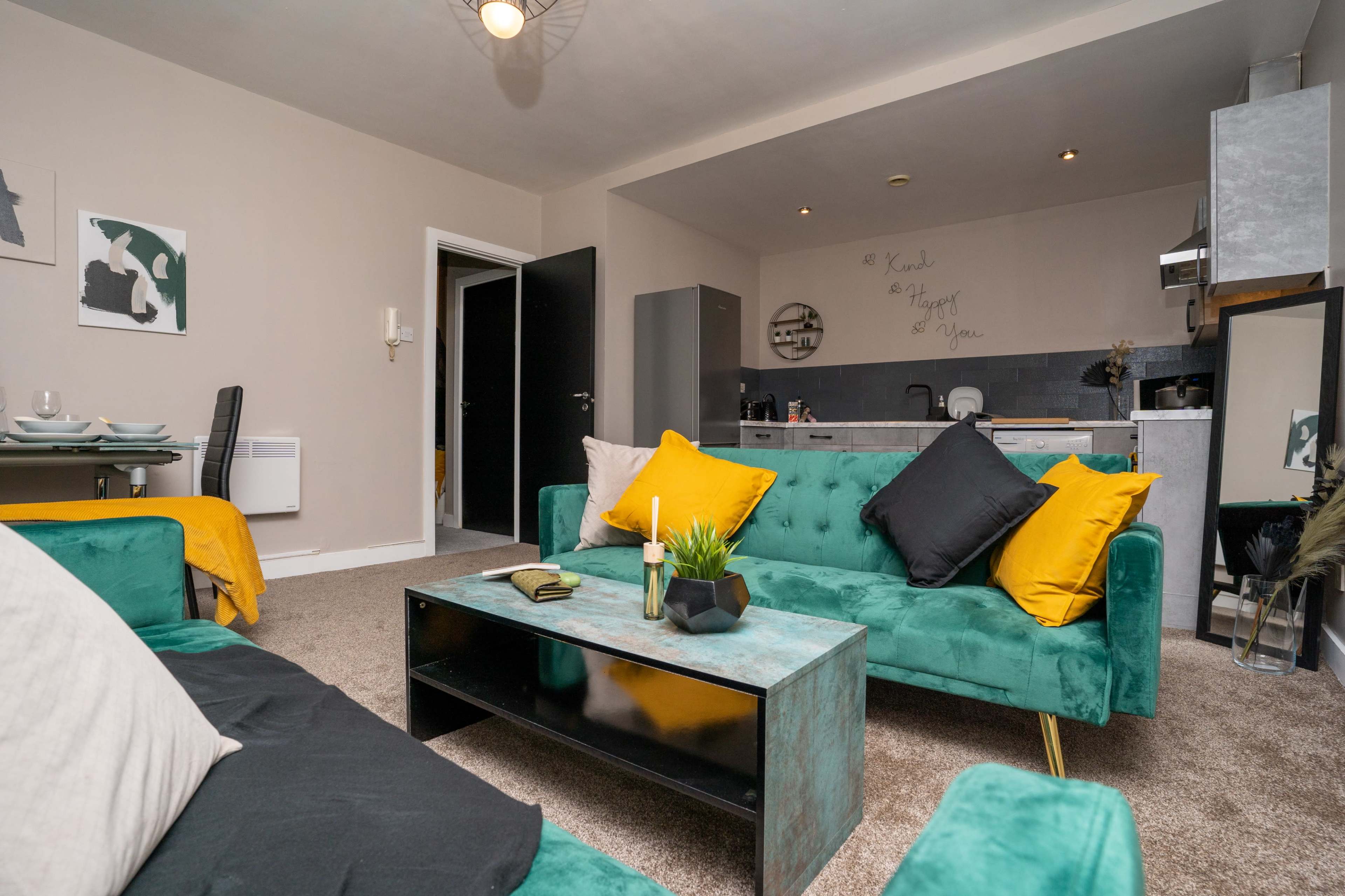 A cozy living room with teal sofas, a black coffee table, and an adjoining kitchen area.
