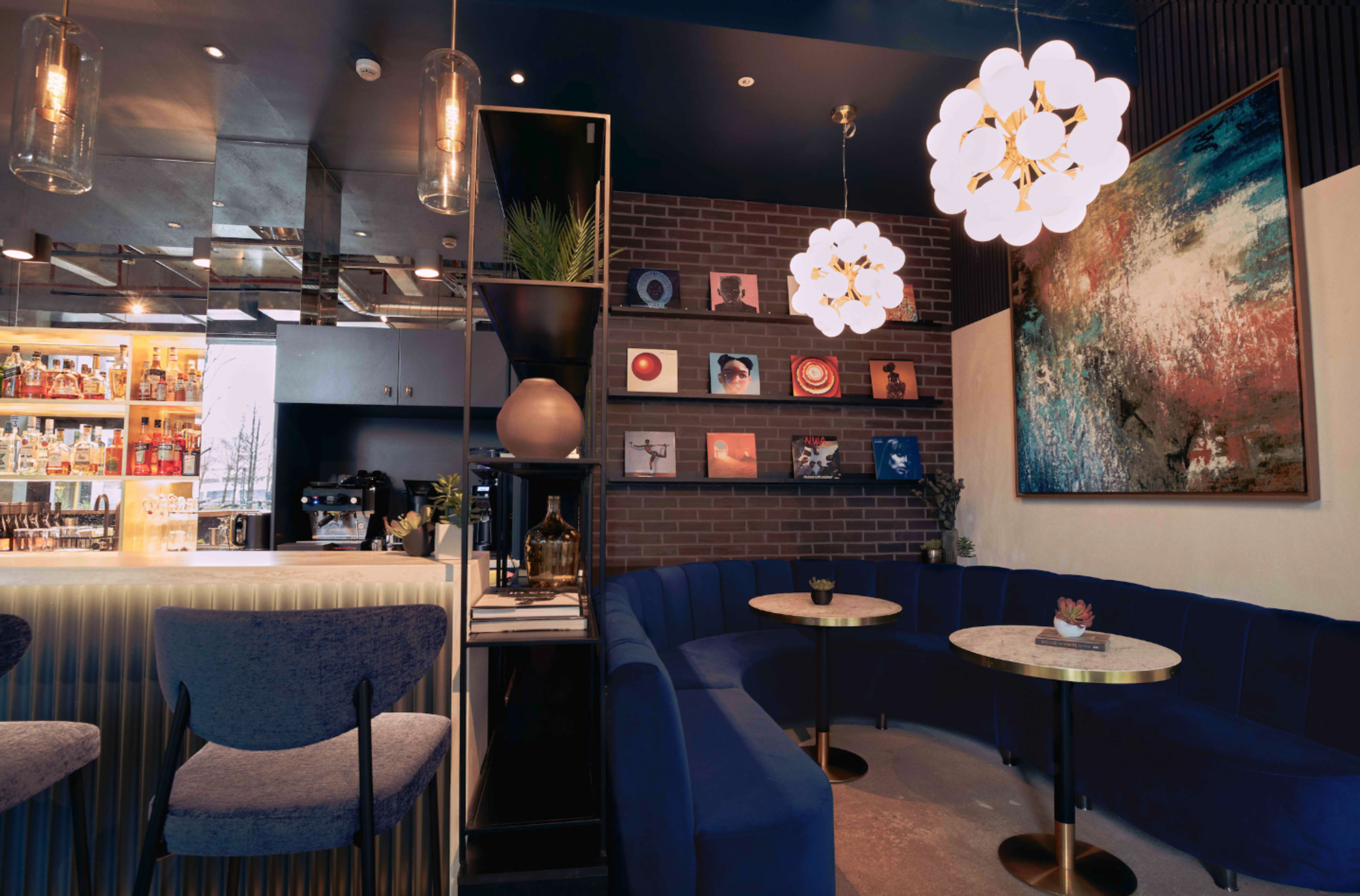 The image shows a modern café interior featuring a blue upholstered seating area, round marble tables, decorative wall art, and stylish light fixtures.