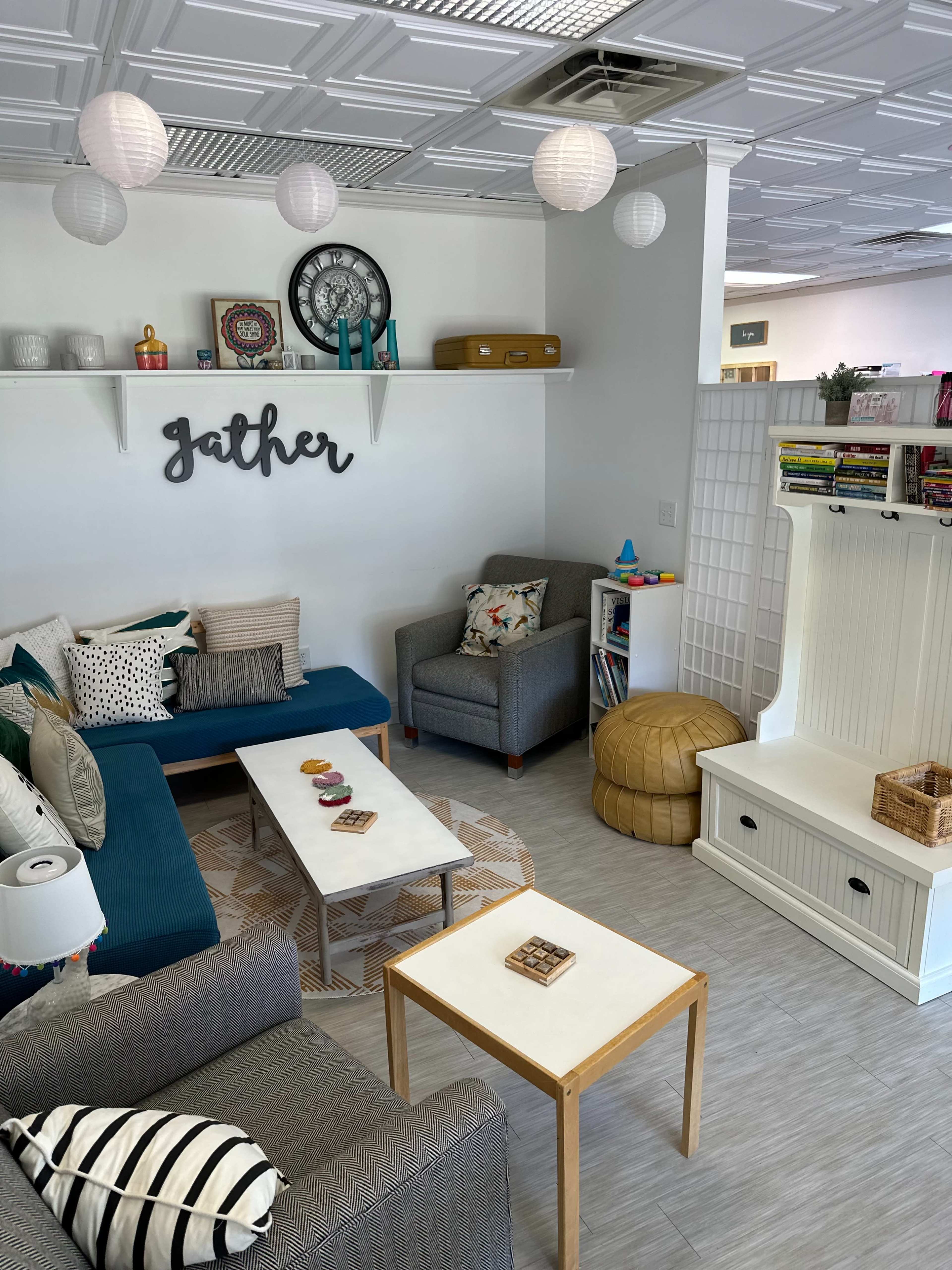 A cozy lounge area with two armchairs, a sectional sofa, several tables, decorative pillows, and a wall that features the word "gather."