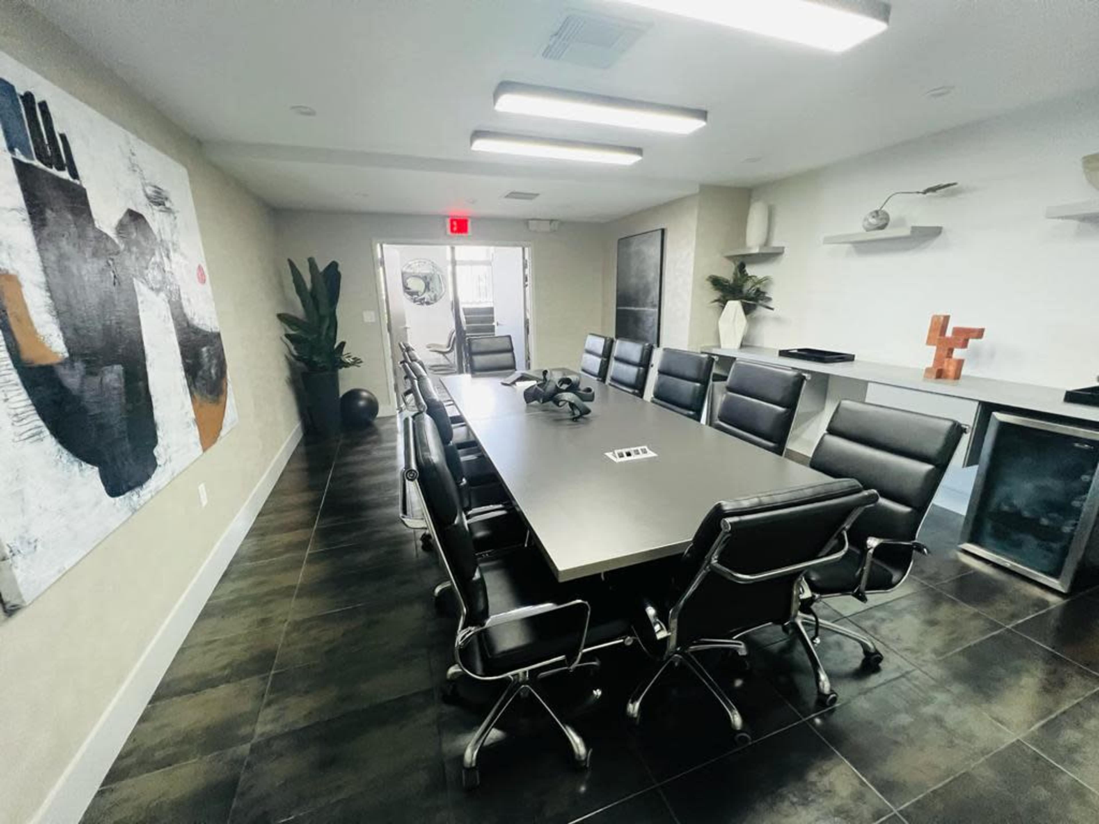 A long conference table surrounded by black leather chairs is featured in a modern meeting room with minimalist decor.
