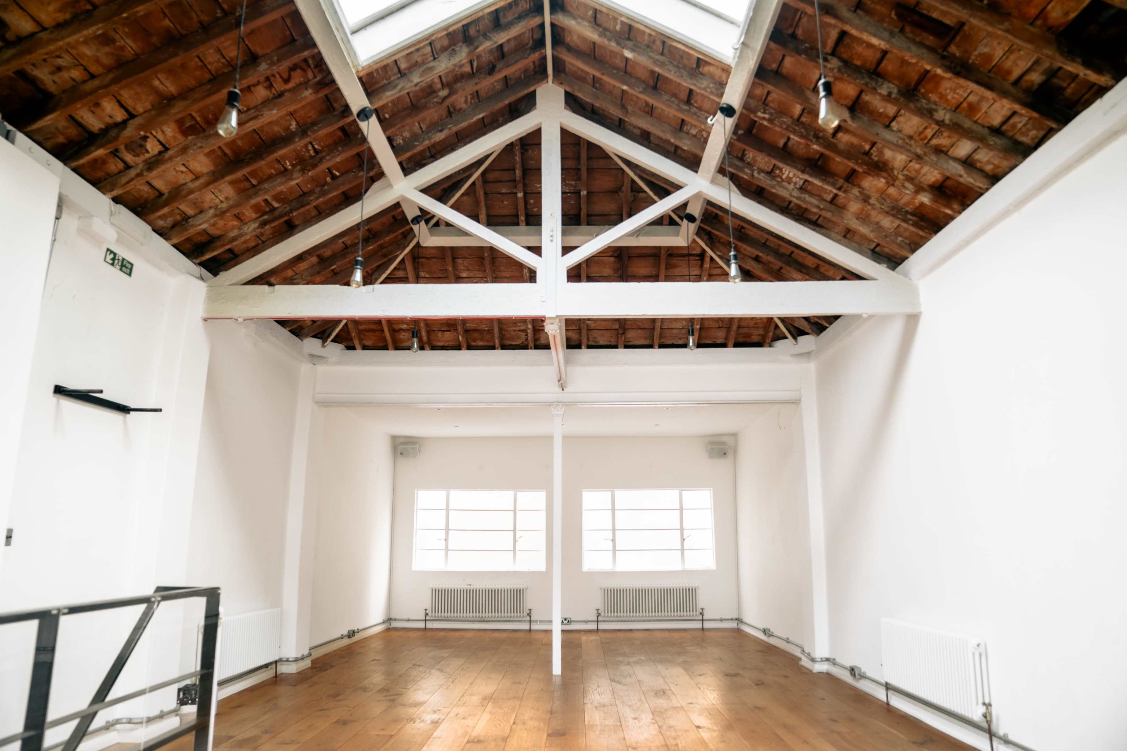 A spacious room with a high, wooden-beamed ceiling and large windows allowing natural light to enter.