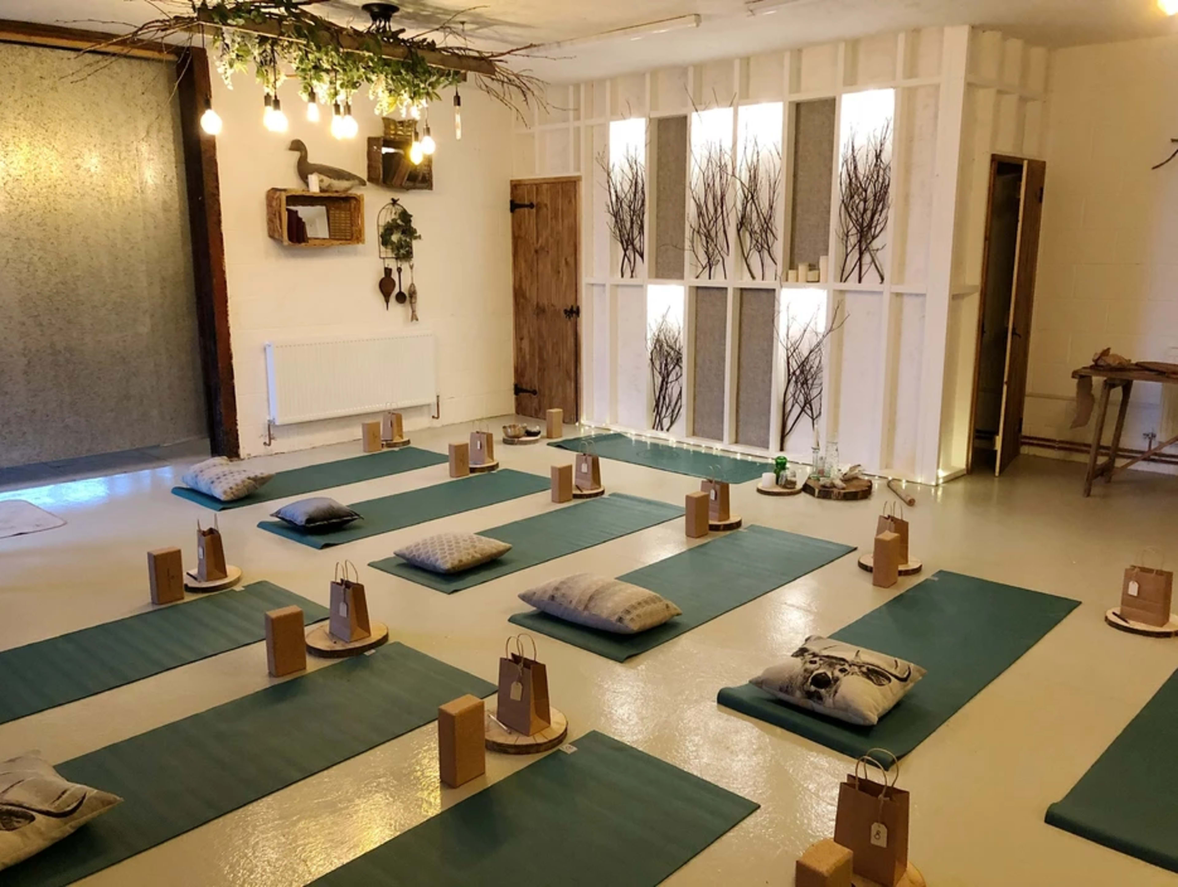 A yoga studio arranged with green mats and cushions for a class, featuring natural decor and warm lighting.