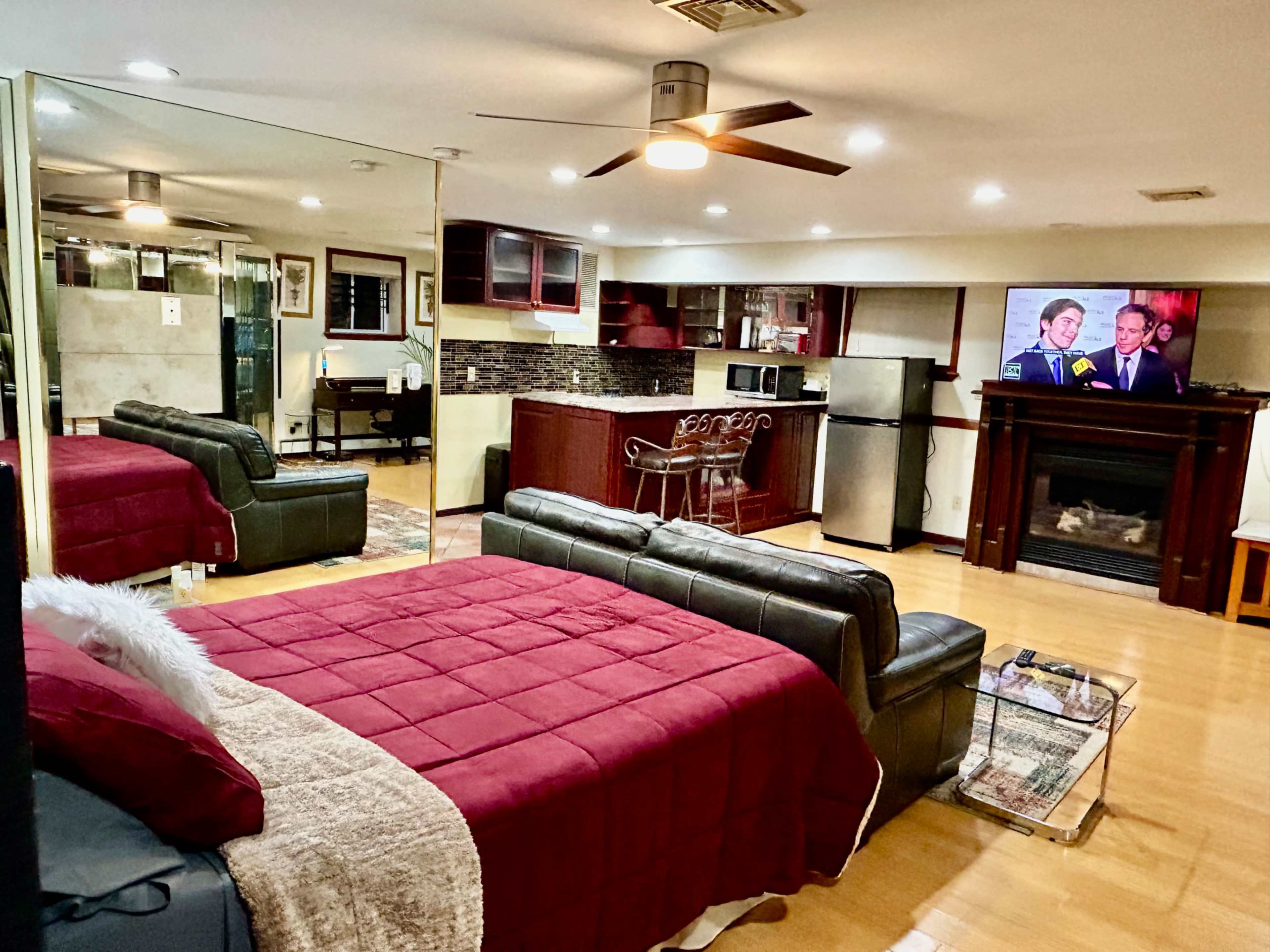 The image depicts a studio apartment with a bed, seating area, kitchen, and a television mounted on the wall.