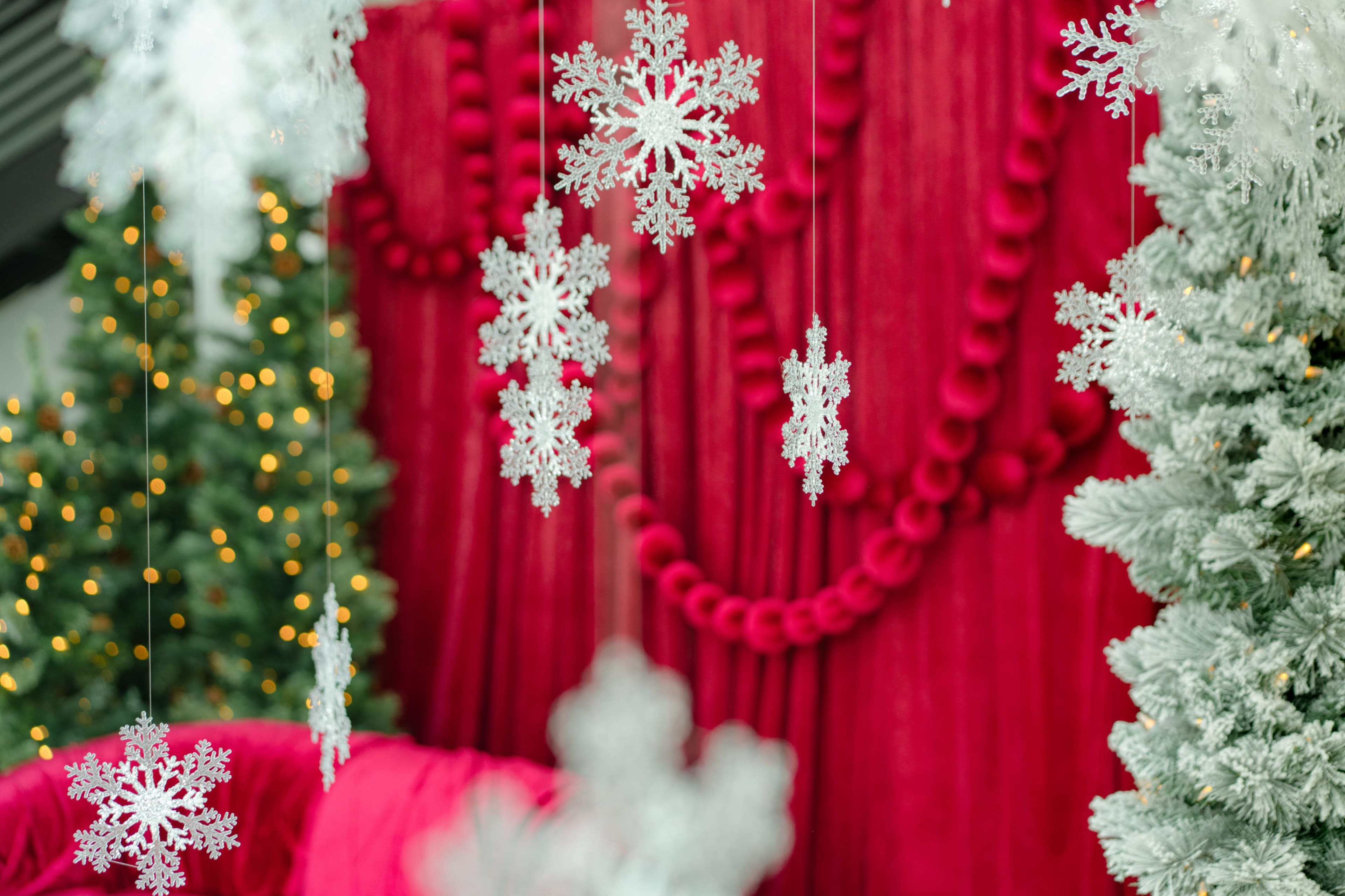 Hanging snowflakes are suspended in front of a red backdrop, adorned with green Christmas trees and twinkling lights.
