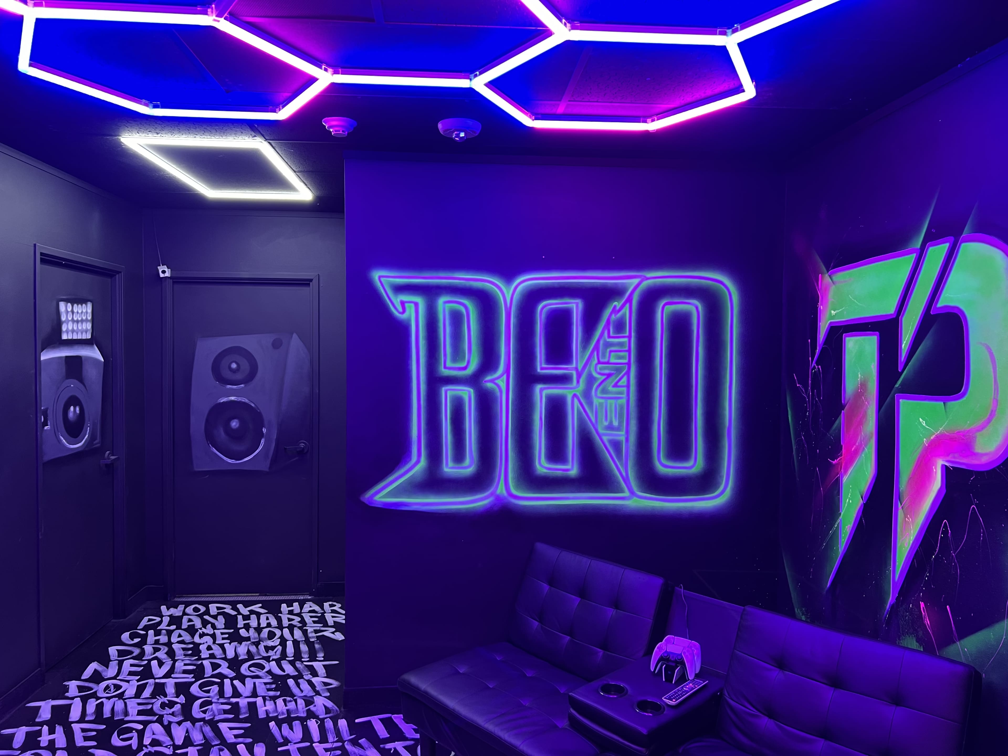 The image shows a modern gaming room with neon lighting, featuring a mural with the text "BEAT" and large speakers on the wall.