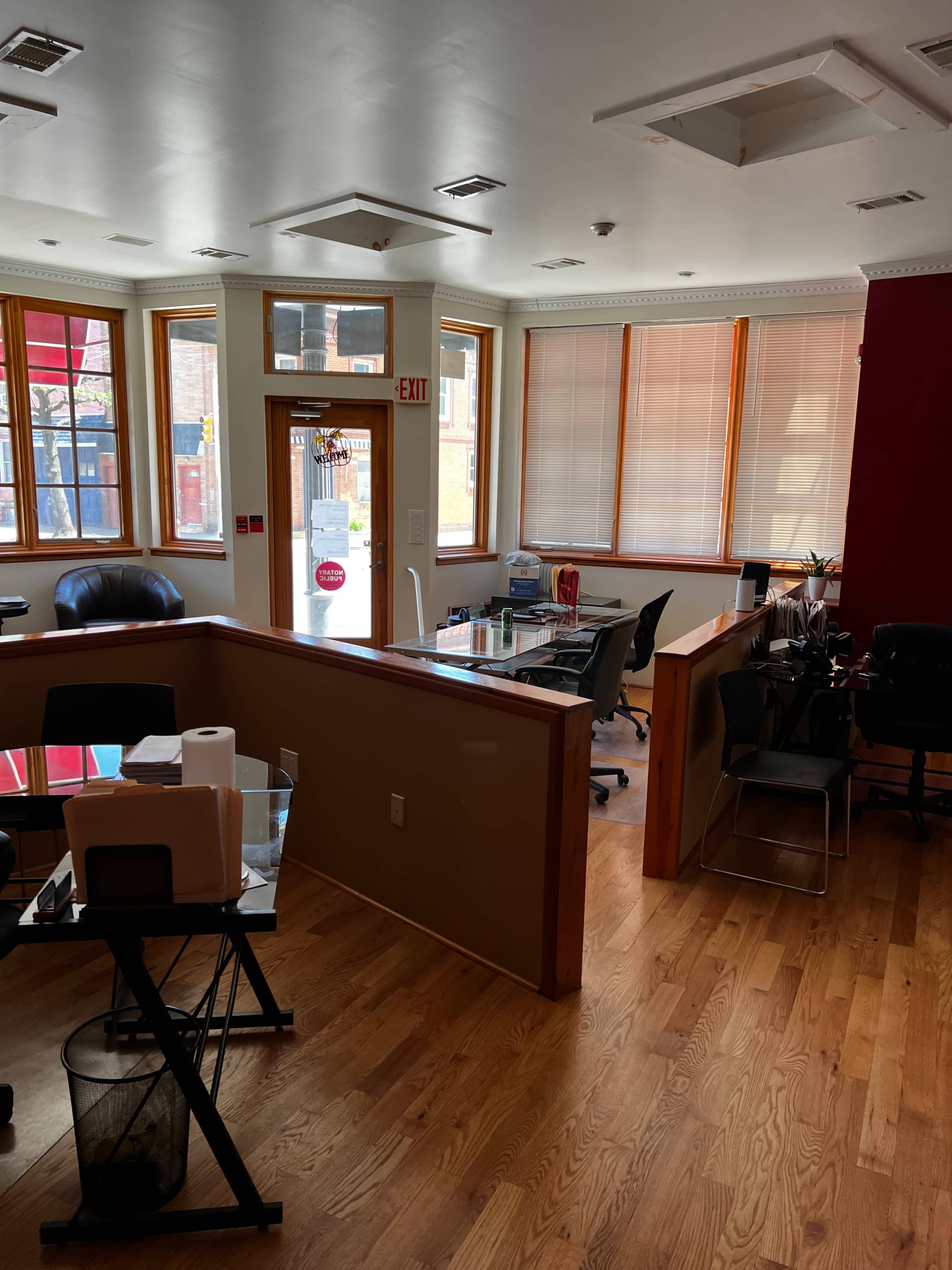 An office space with hardwood floors, large windows allowing natural light, and various workstations including desks and chairs.